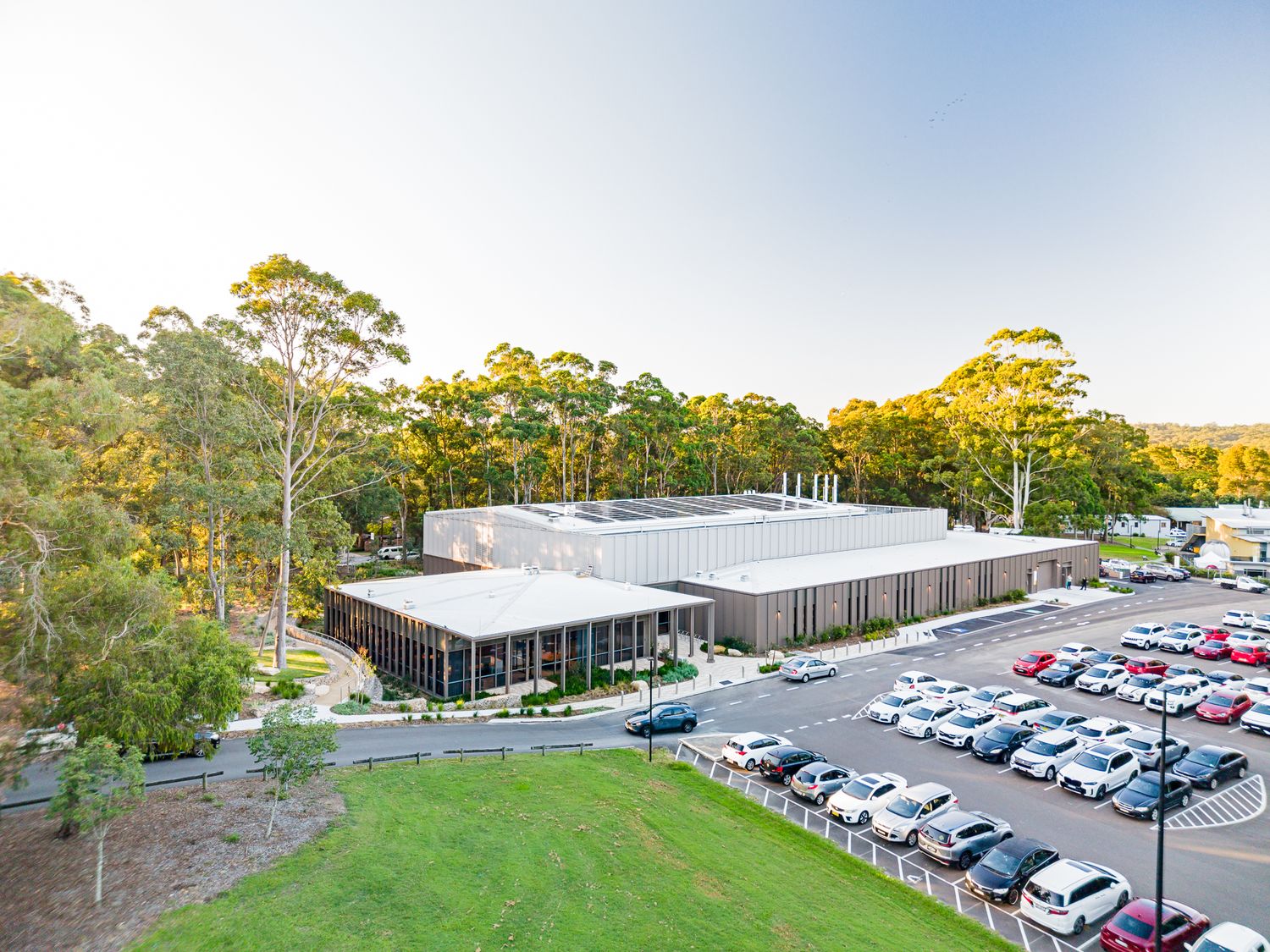 Aerial view of a modern biomanufacturing facility surrounded by eucalyptus trees with a large car park and green lawn.