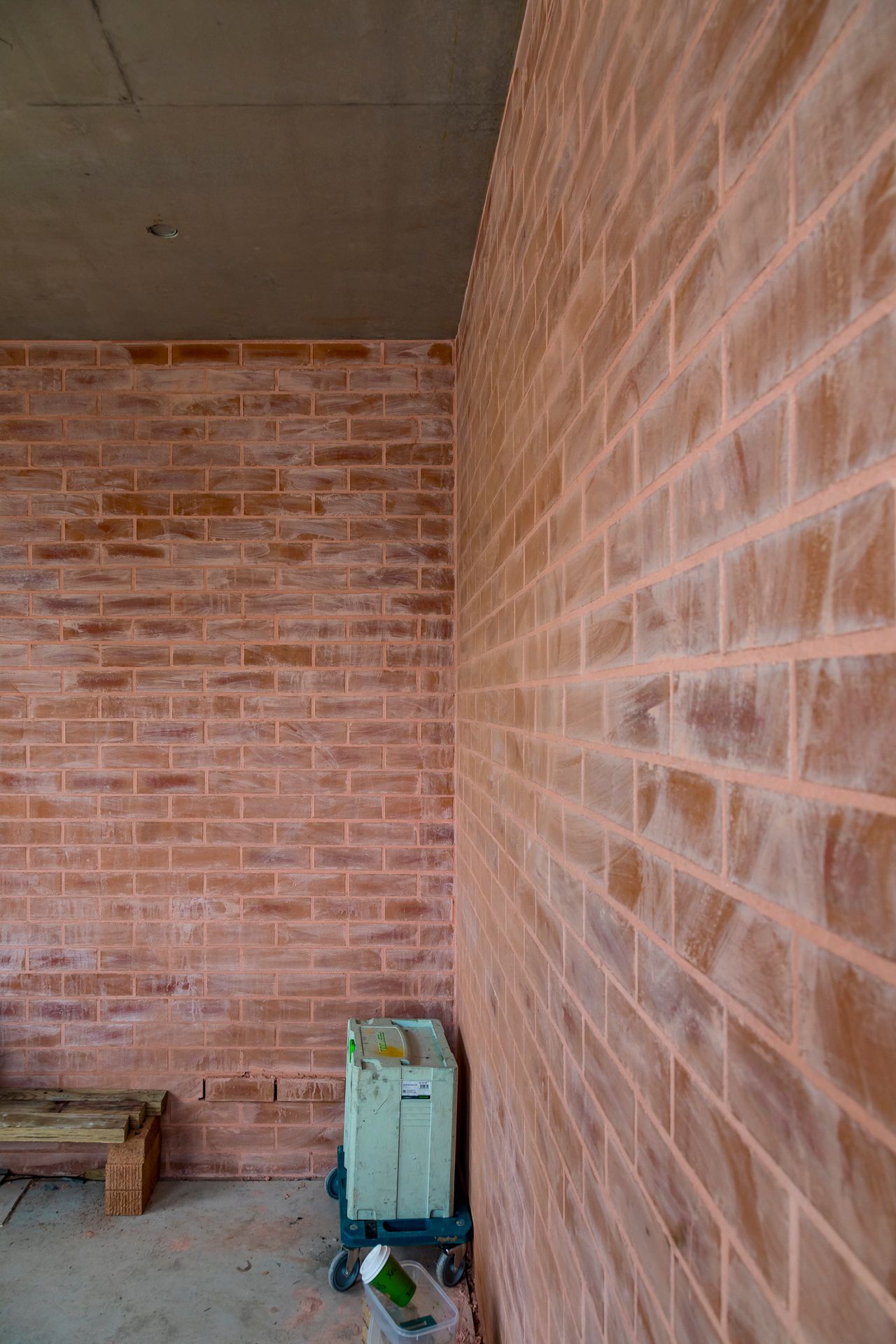 Corner of an unfinished room with pink-toned brick walls, a concrete ceiling and a portable site cart on the floor.