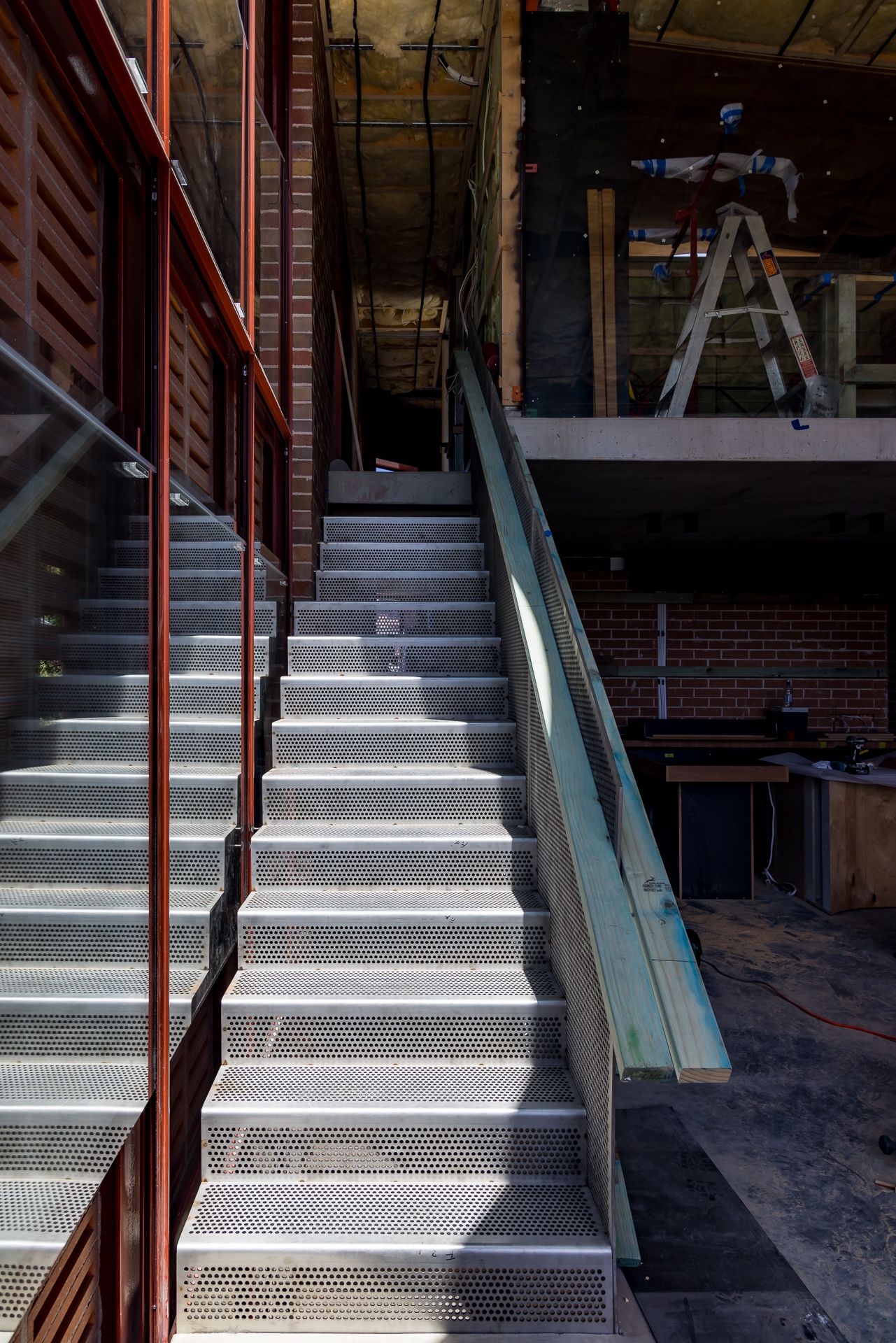 Perforated metal staircase with steel handrail inside a brick building under construction.