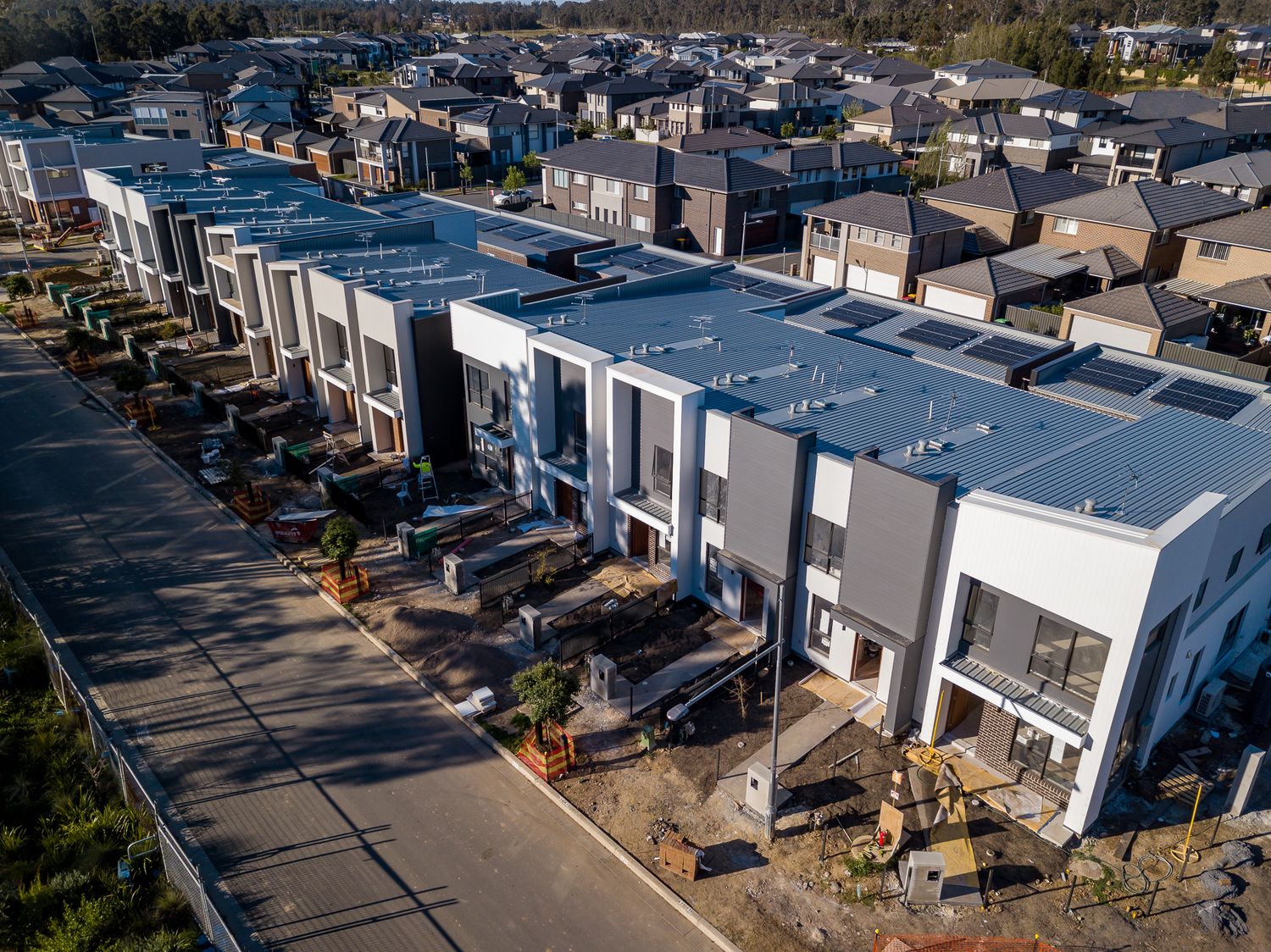 Aerial view of a modern row of white and grey townhouses with flat roofs and solar panels in a new residential estate.