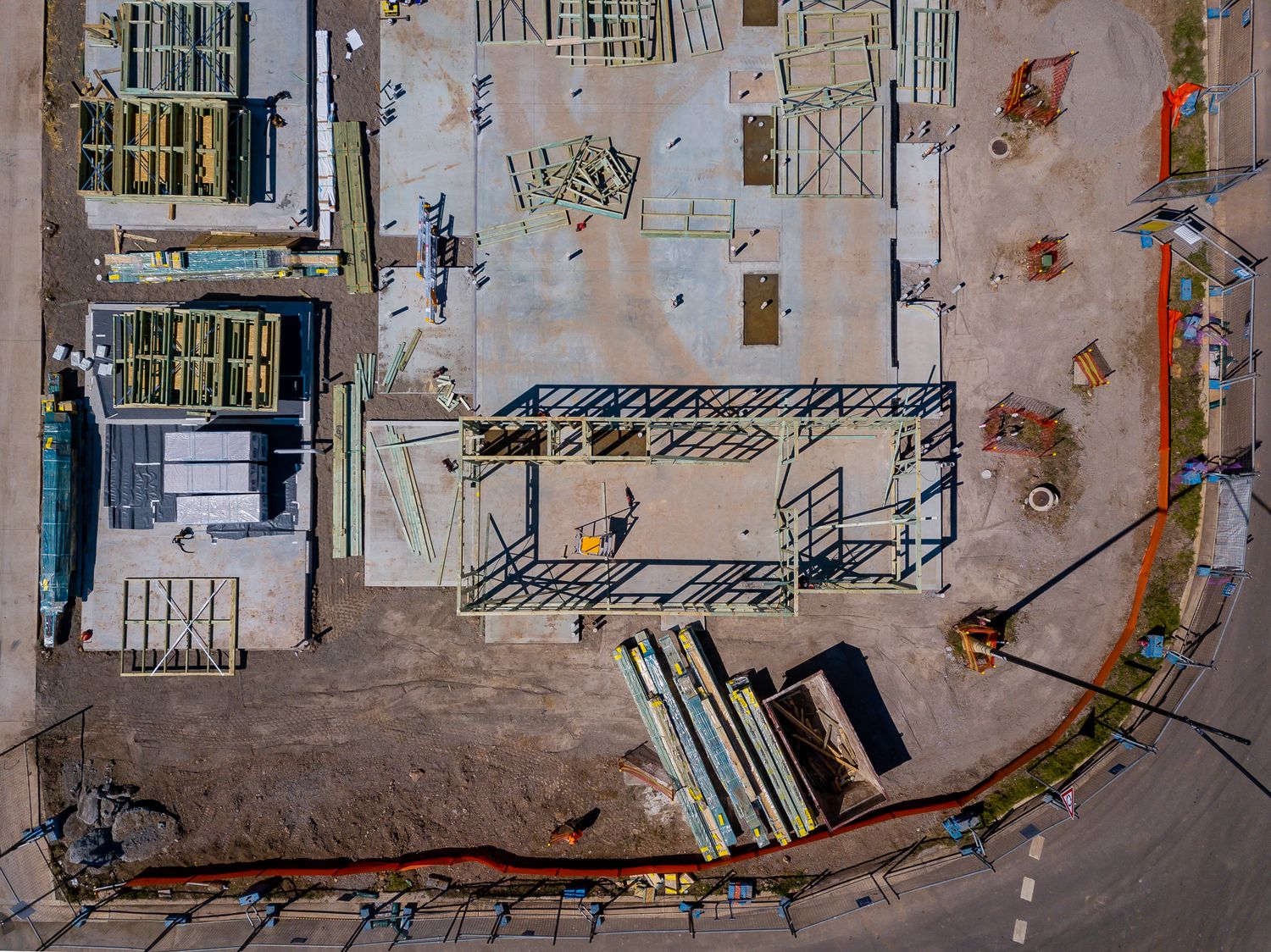 Top-down drone view of a construction site with a partially built steel frame, building materials, and bare dirt ground.