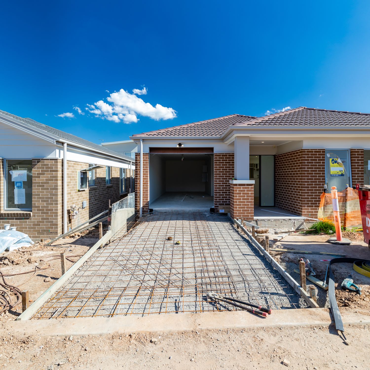 New brick house under construction with a steel-reinforced concrete driveway, garage and tiled roof on a sunny day.