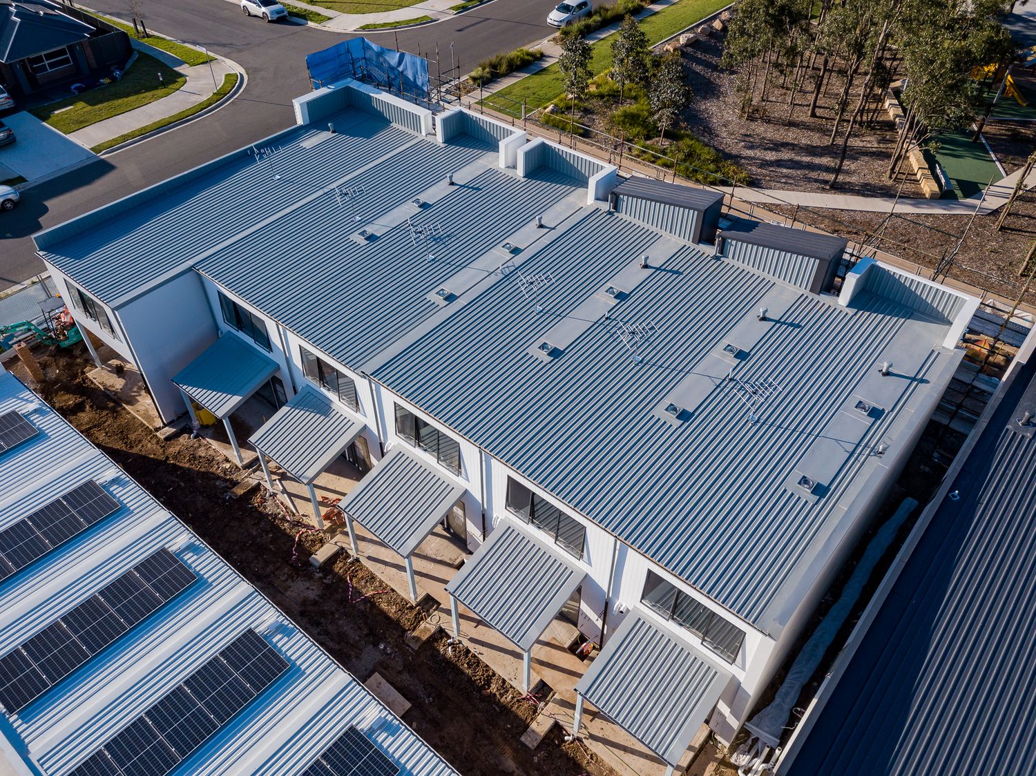 Aerial view of a new townhouse development with metal roofing, solar panels and a neighbouring street.