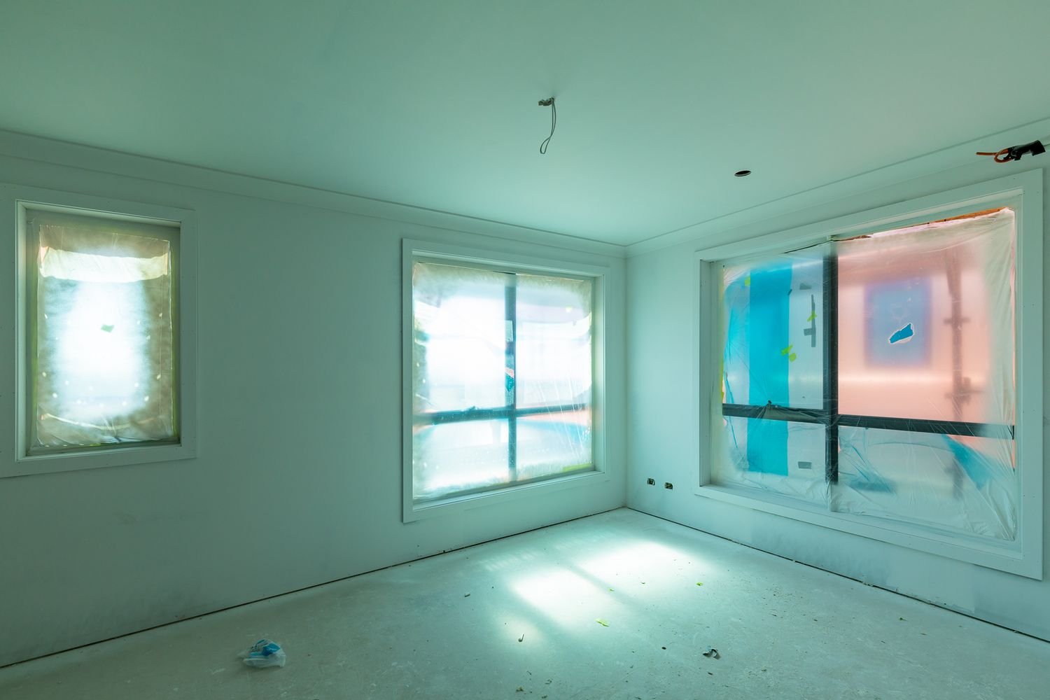 Empty bedroom under construction with plastered walls, large windows covered in protective film and a bare, dusty floor.