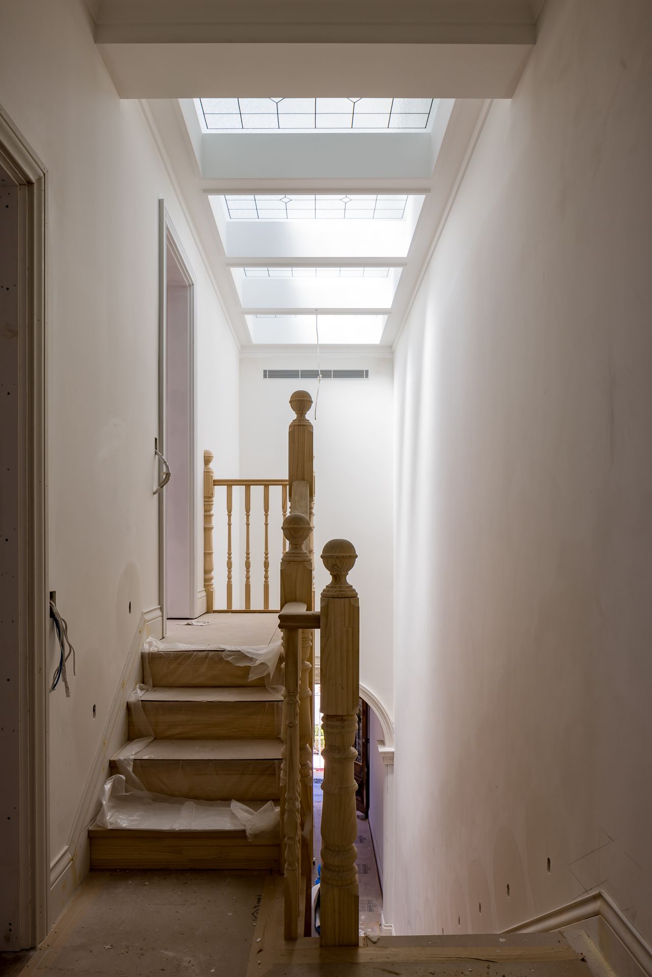 Unfinished timber staircase with protective wrapping on the steps, turned newel posts and a bright skylight above during a home renovation.