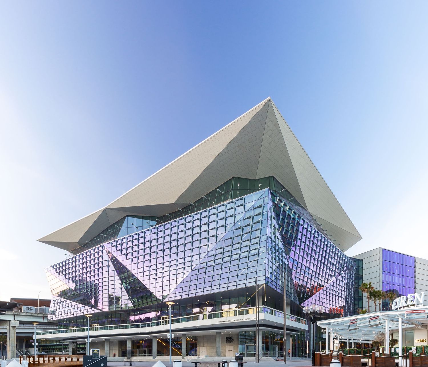 Angular convention centre with a pointed roof and faceted glass facade rising above a waterfront promenade.