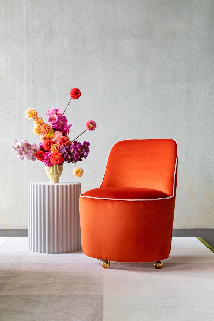 Orange velvet armchair with white piping beside a ribbed white side table holding a bouquet of pink and orange dahlias.