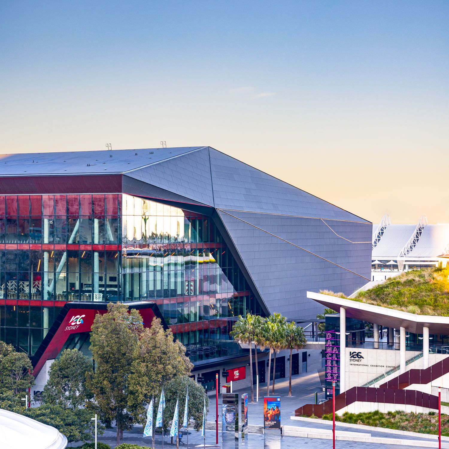 Angular glass and steel ICC theatre with red accents and a rooftop garden glowing at sunset.
