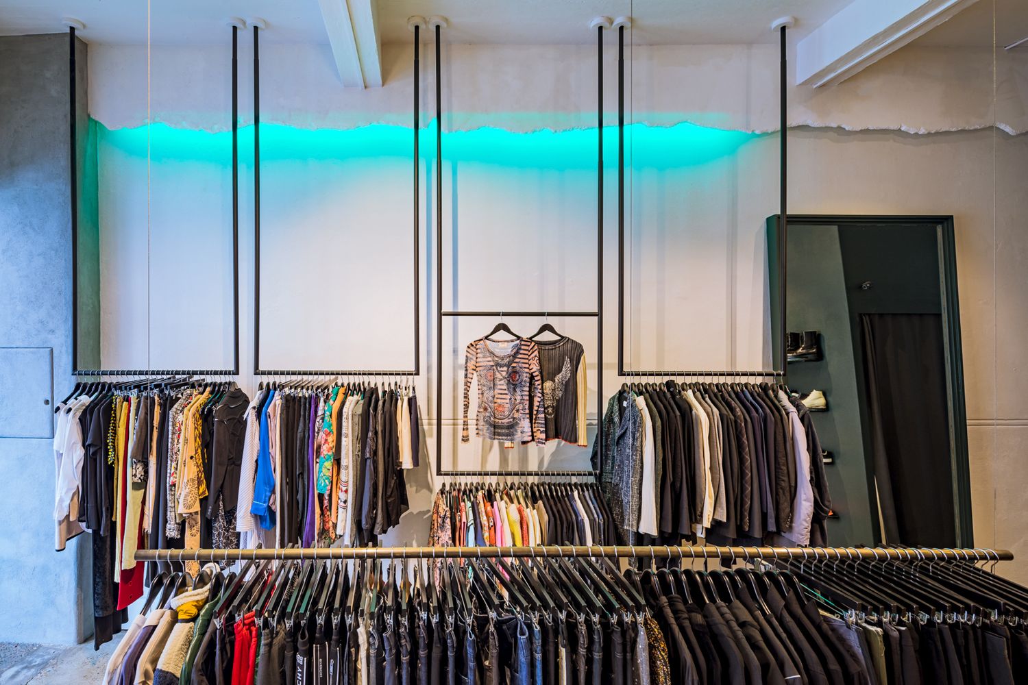 Boutique clothing store with garments on hanging rails, glowing teal neon lighting and a concrete-style wall.