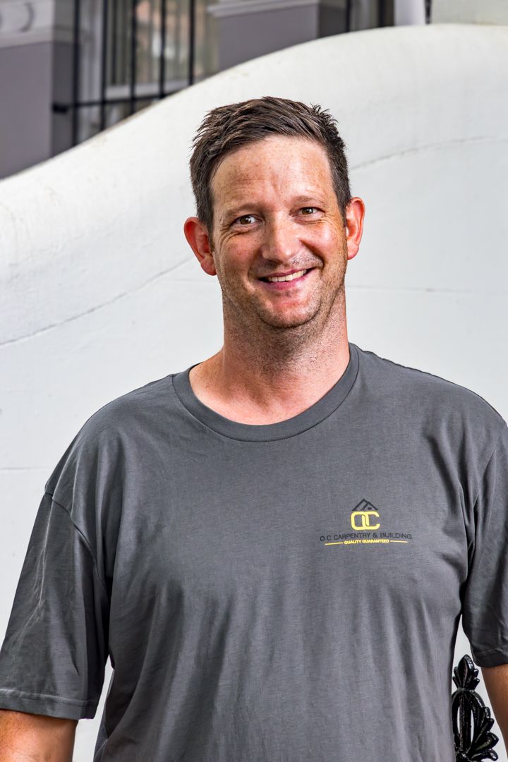 A smiling man in a gray company t-shirt poses for a close-up portrait in front of a white curved wall.