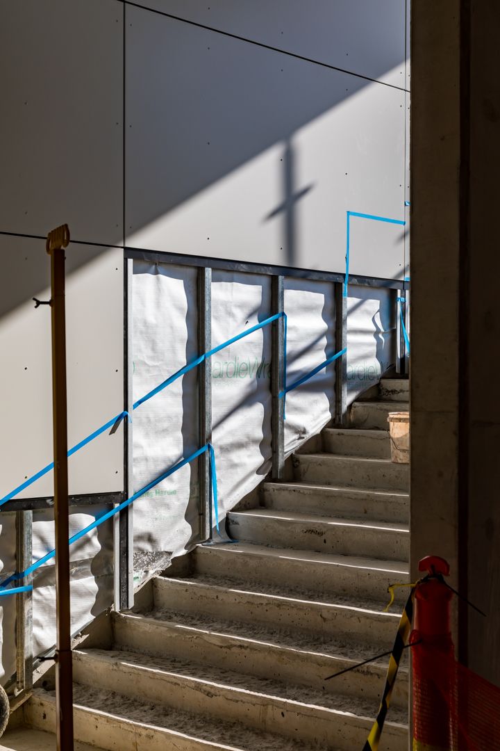 Concrete staircase in a building under construction with blue-taped wrap on the walls and safety barriers in strong sunlight.