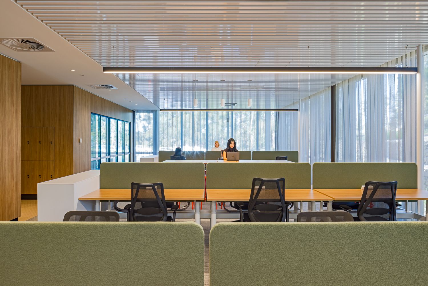 Quiet study area with green upholstered seating, wooden panelling and floor-to-ceiling windows looking out to the bushland.