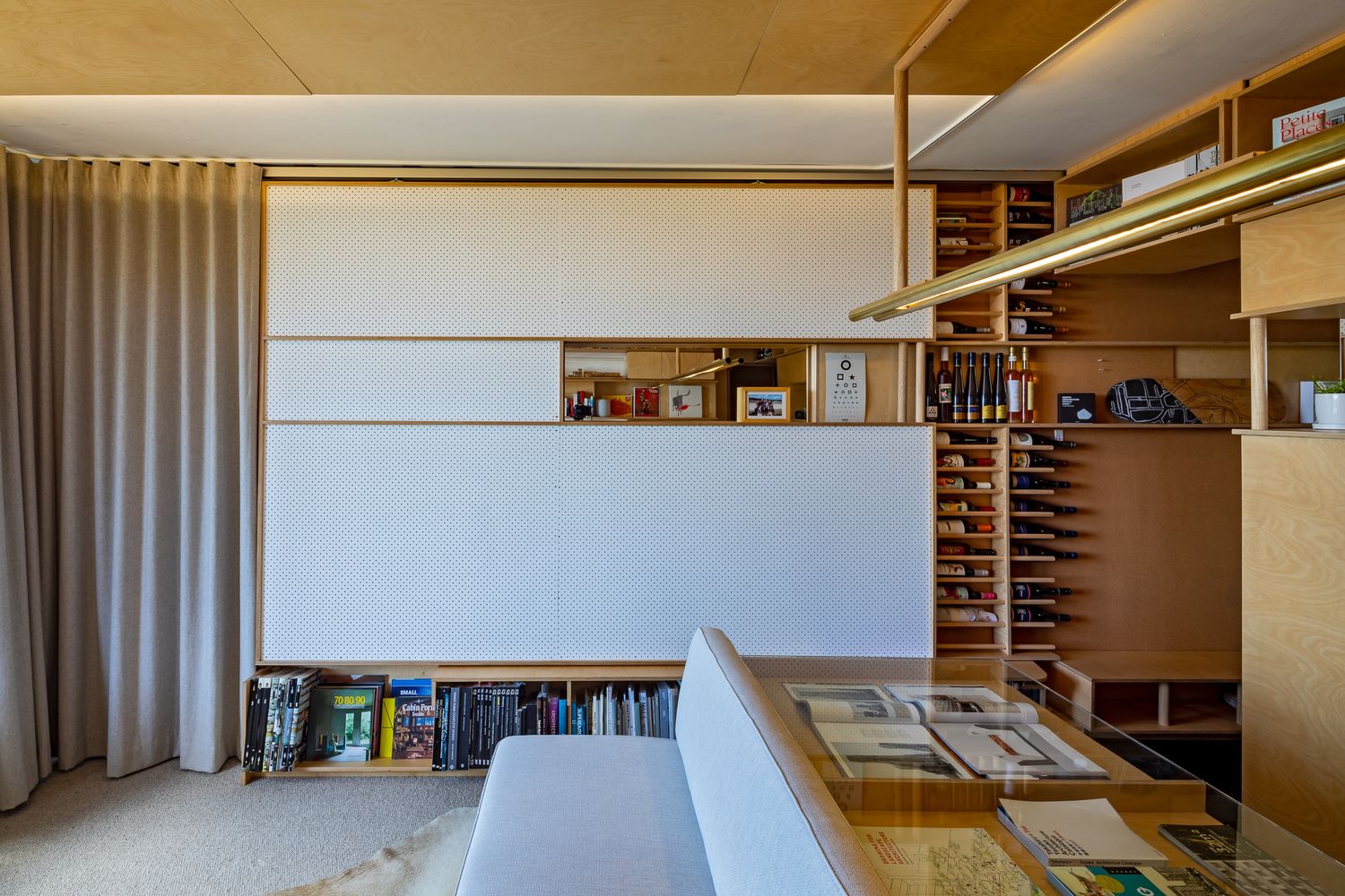 Closed white sliding panels cover the entertainment wall, with open wooden shelves and a low bookshelf below.