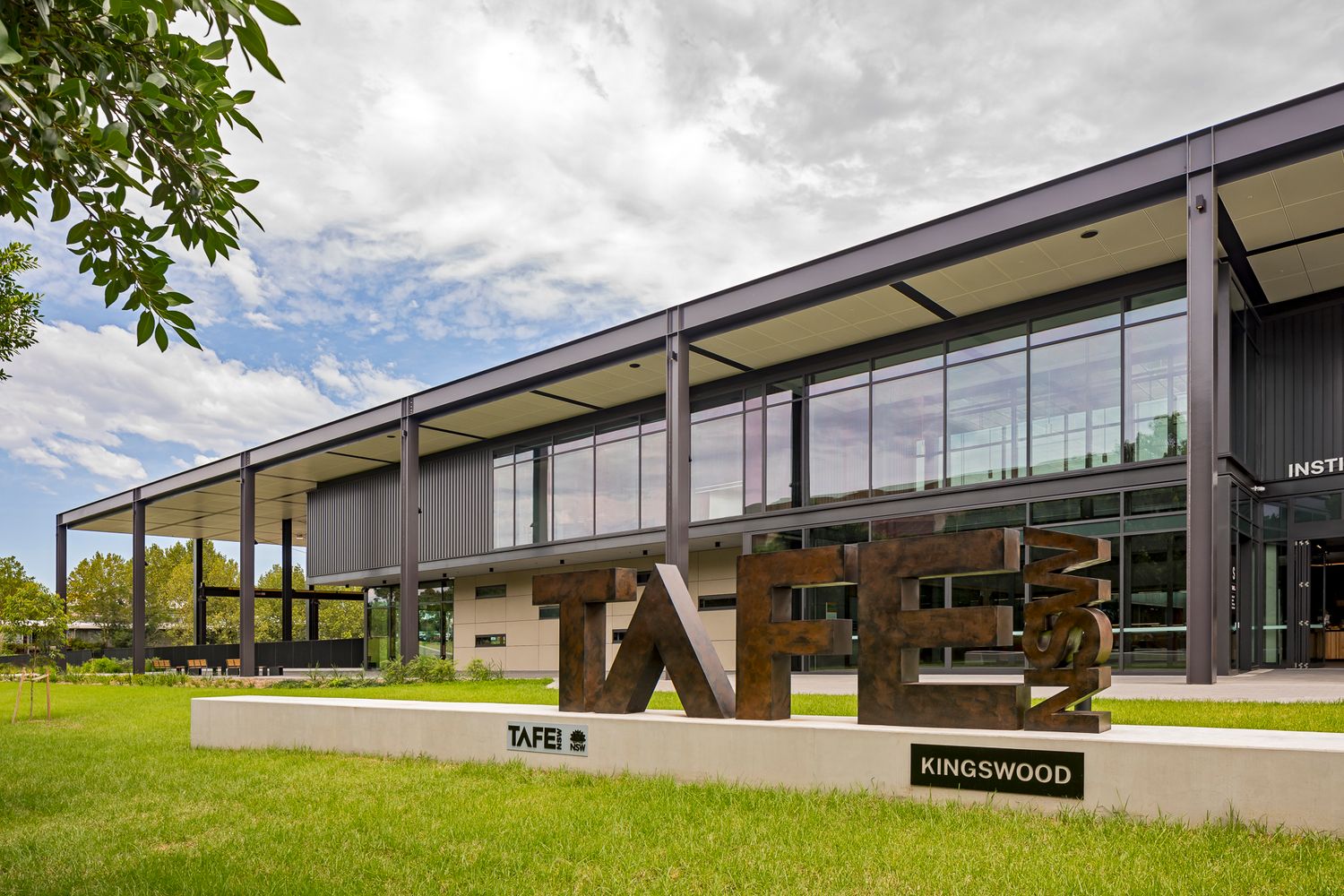 Modern TAFE Kingswood campus building with large glass windows, steel columns and bold rust-colored lettering above a green lawn.