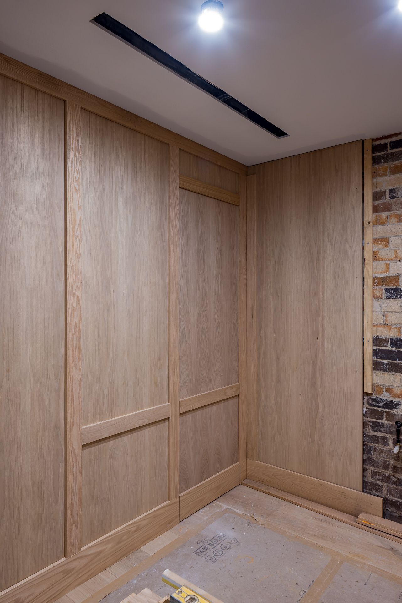 Corner of a renovation project with new oak timber wall panelling, exposed original brick, a recessed ceiling light and a linear vent.