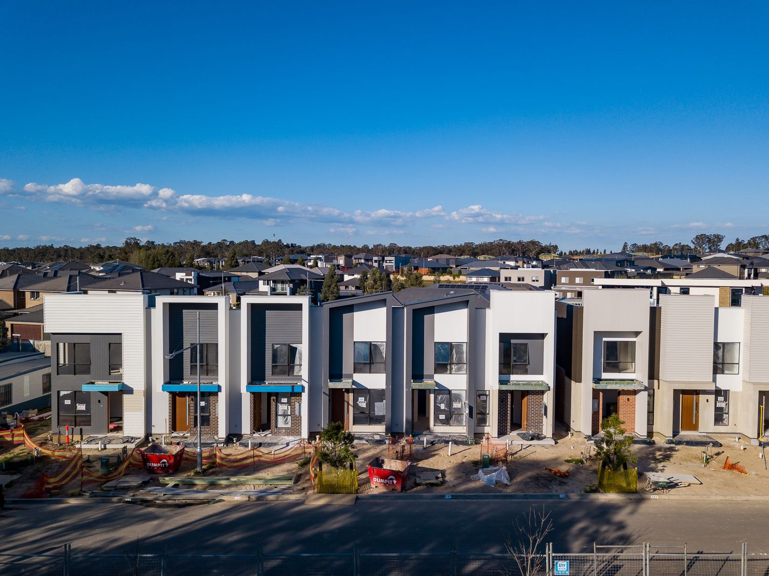 Row of modern multi-storey townhouses with white and grey facades and blue awnings, standing under a clear blue sky.