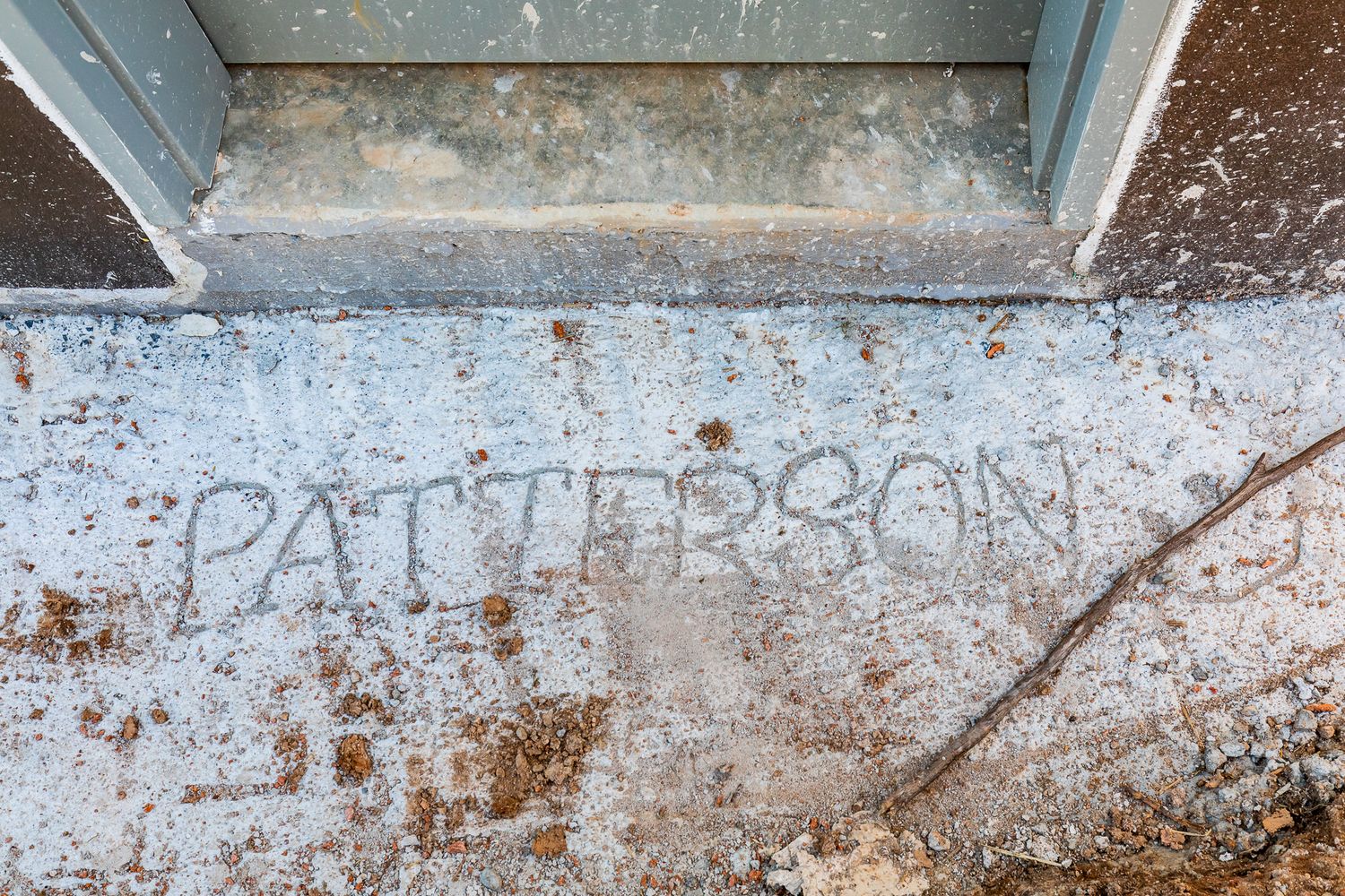 Name Patterson scratched into a concrete slab beside a door threshold at a building site.