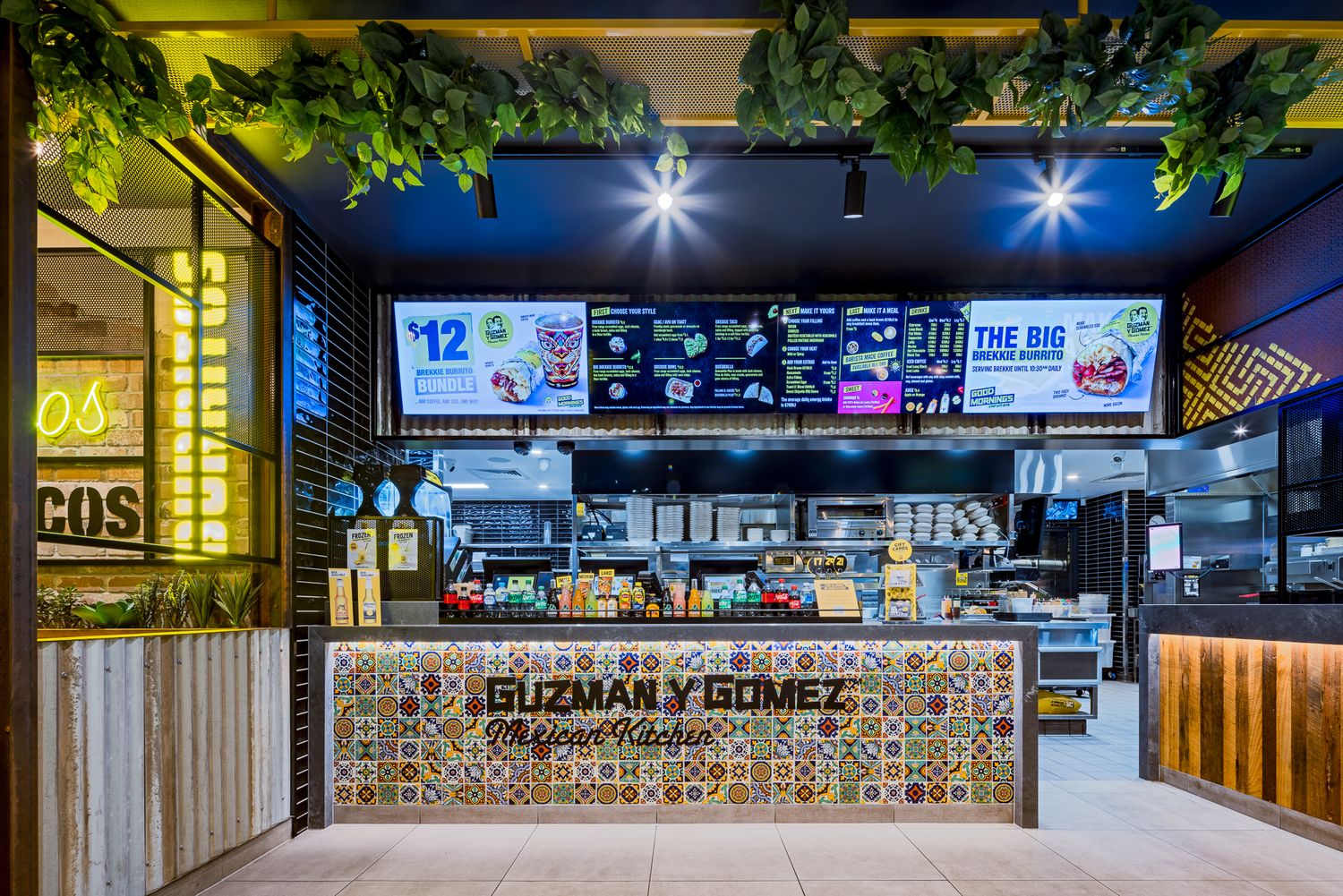 Guzman y Gomez ordering counter with mosaic tile front, overhead digital menus and warm timber accents in a mall food court.