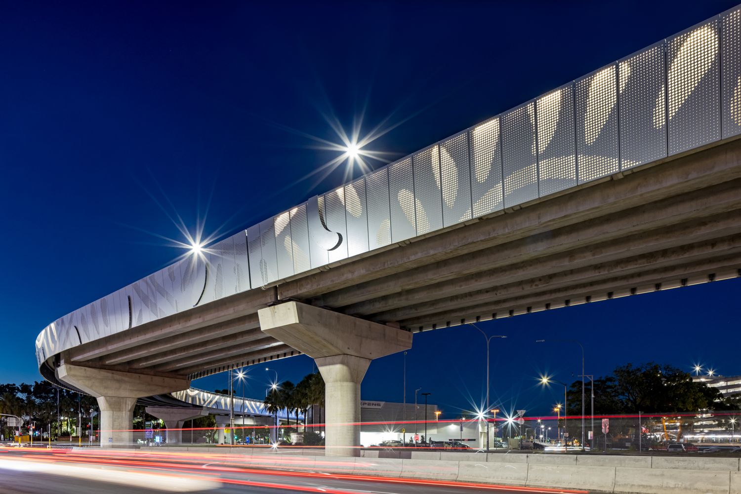 Elevated roadway with a perforated decorative barrier and concrete support columns lit against a deep blue night sky.