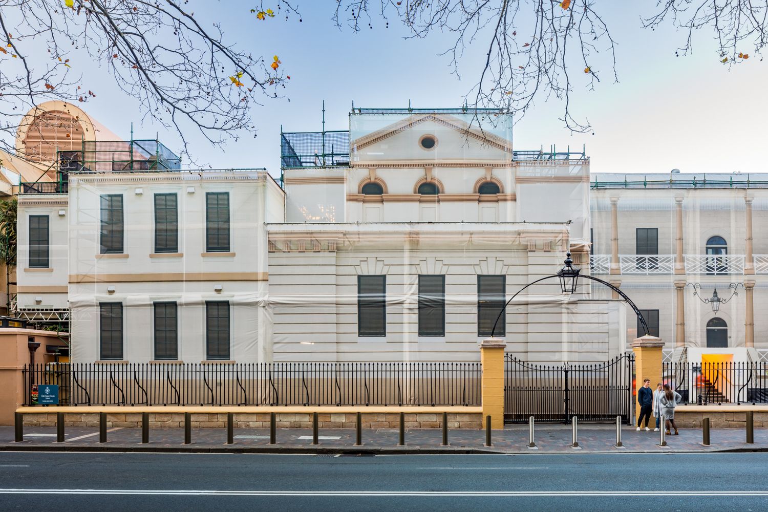 Historic cream-colored heritage building with arched windows and protective fencing along a city street during restoration works.