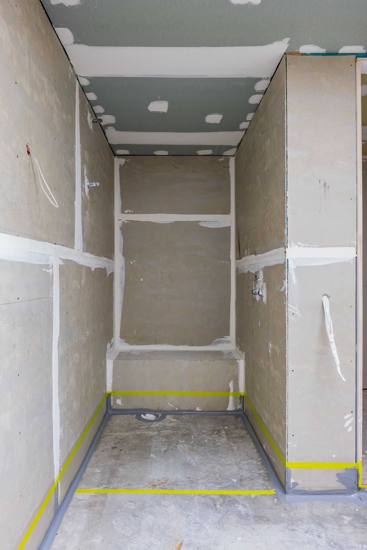 Unfinished shower recess in a bathroom renovation with plasterboard walls, waterproofing tape and a floor drain.