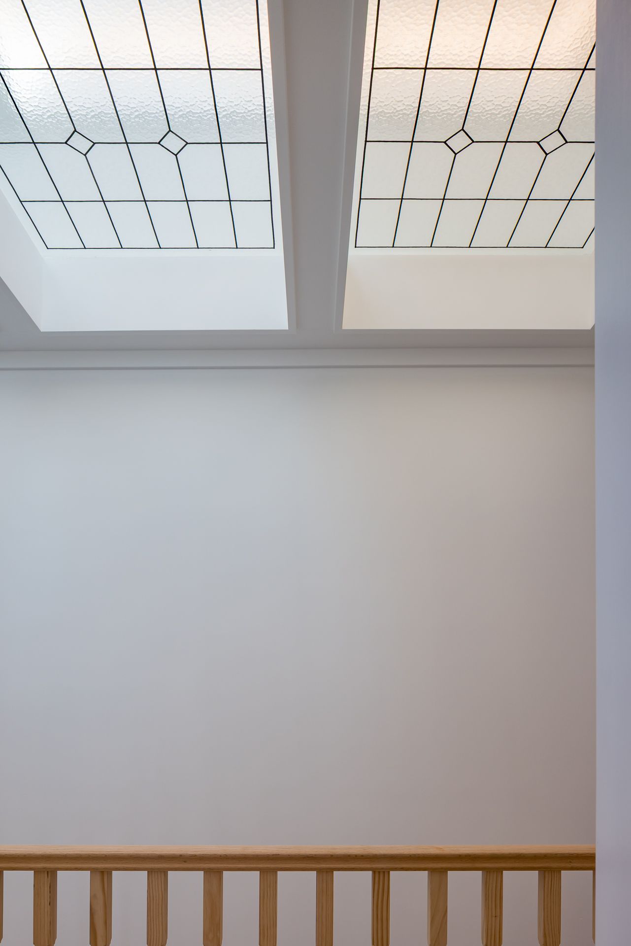 Two skylights with leadlight-style glass in a diamond pattern above a white wall and timber balustrade in a bright stairwell.
