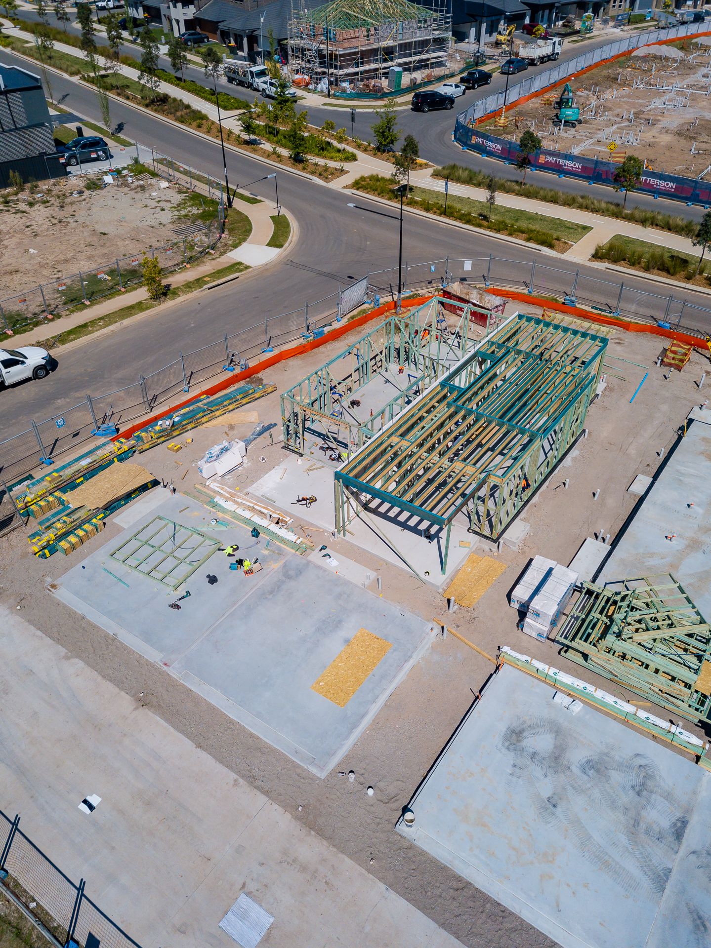 Aerial view of house frames and concrete slabs on a residential building site beside a curved road in a new housing development.