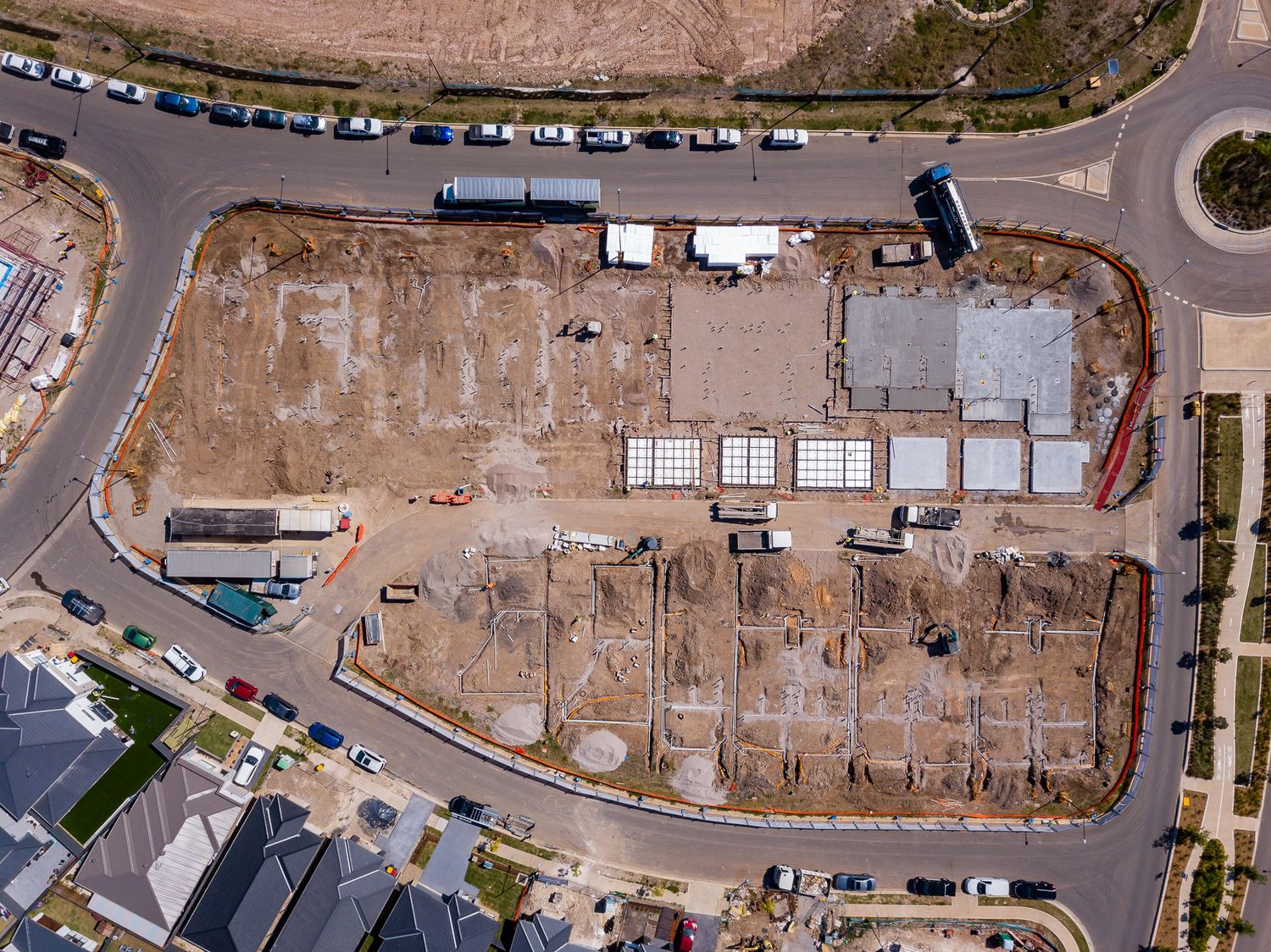 Top-down aerial view of a residential construction site with building foundations and slabs beside a roundabout and a nearby road.
