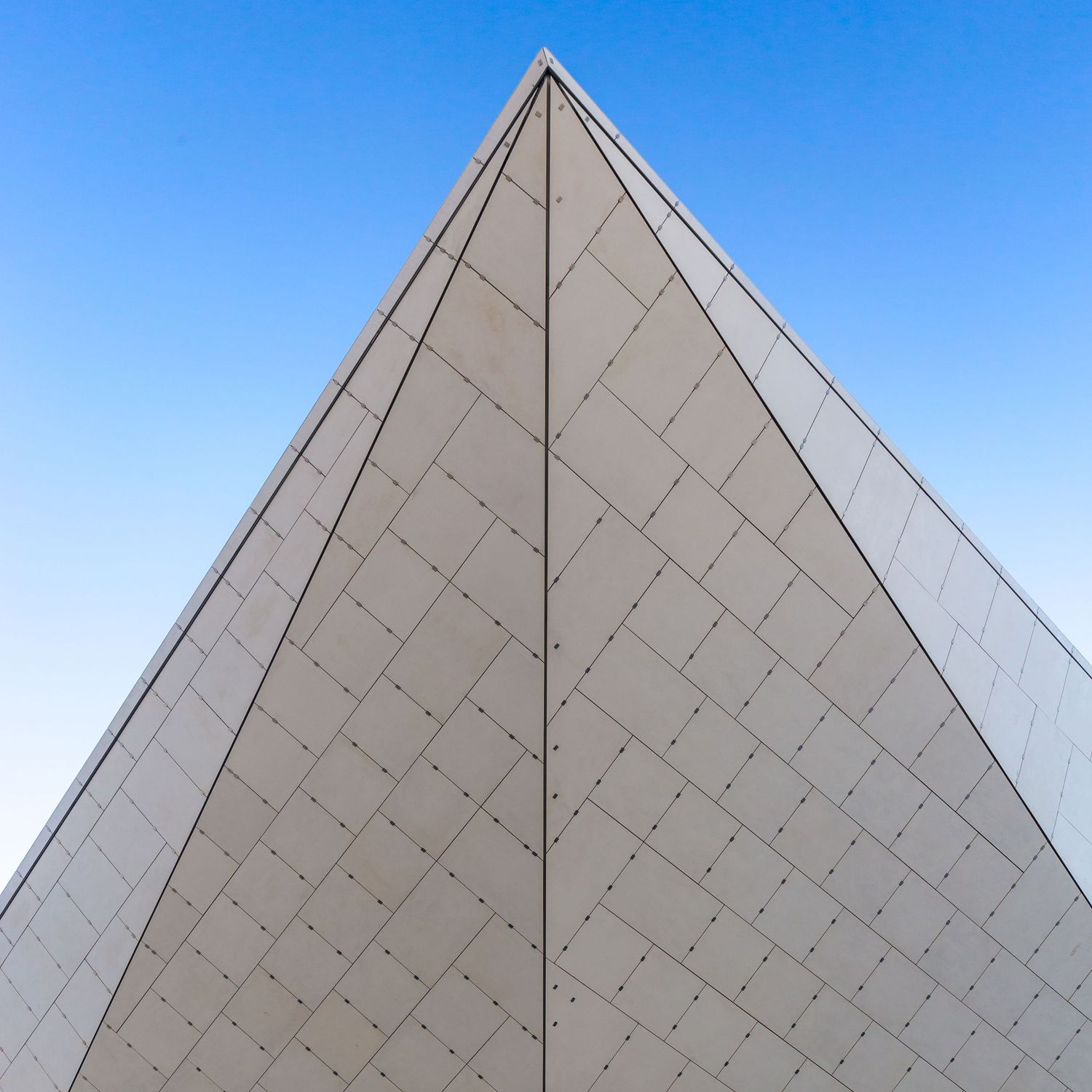 Sharp upward view of a white tiled building corner meeting a deep blue sky.
