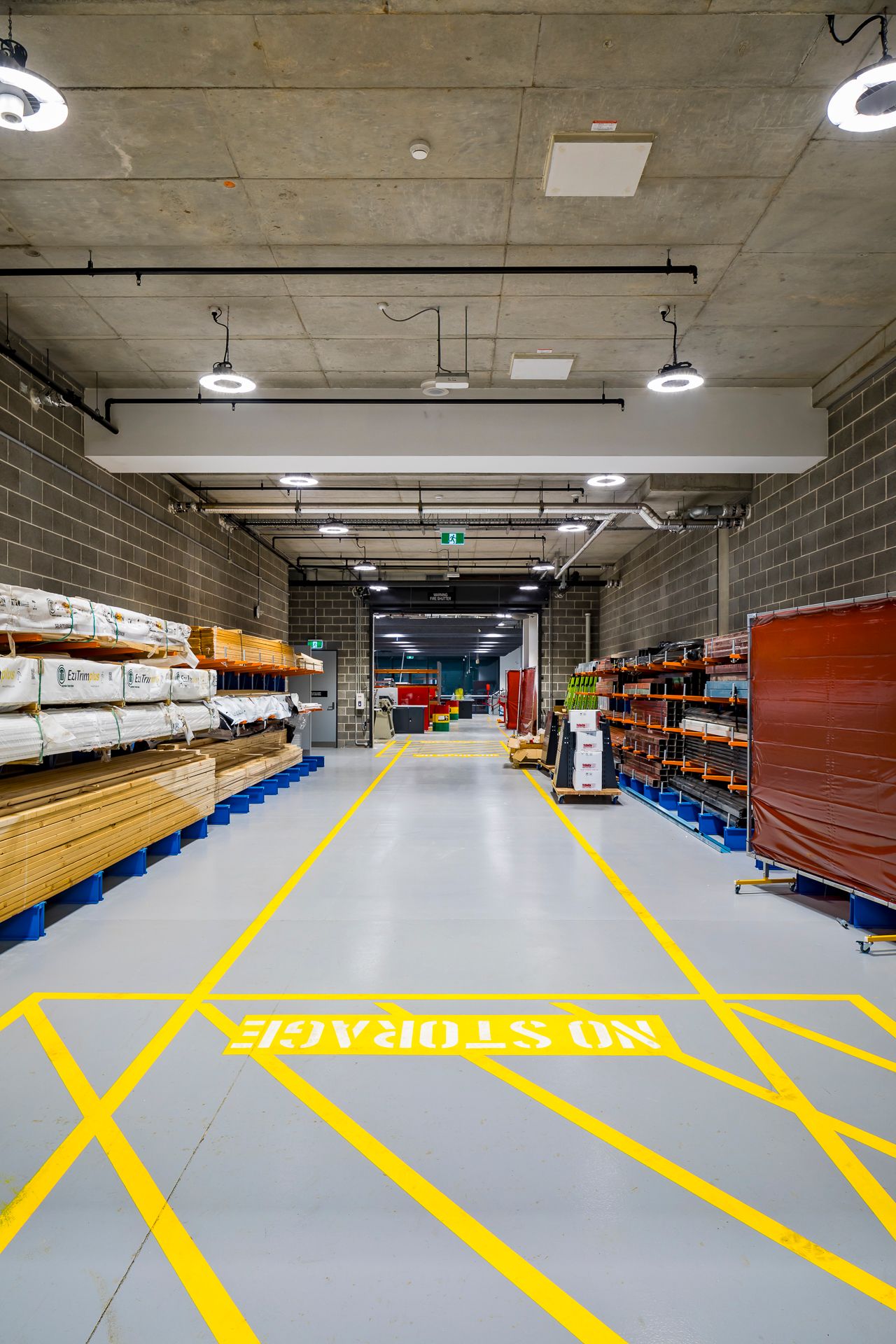 Tidy materials storage corridor with yellow safety markings, a No Storage floor sign and shelves of timber and supplies.