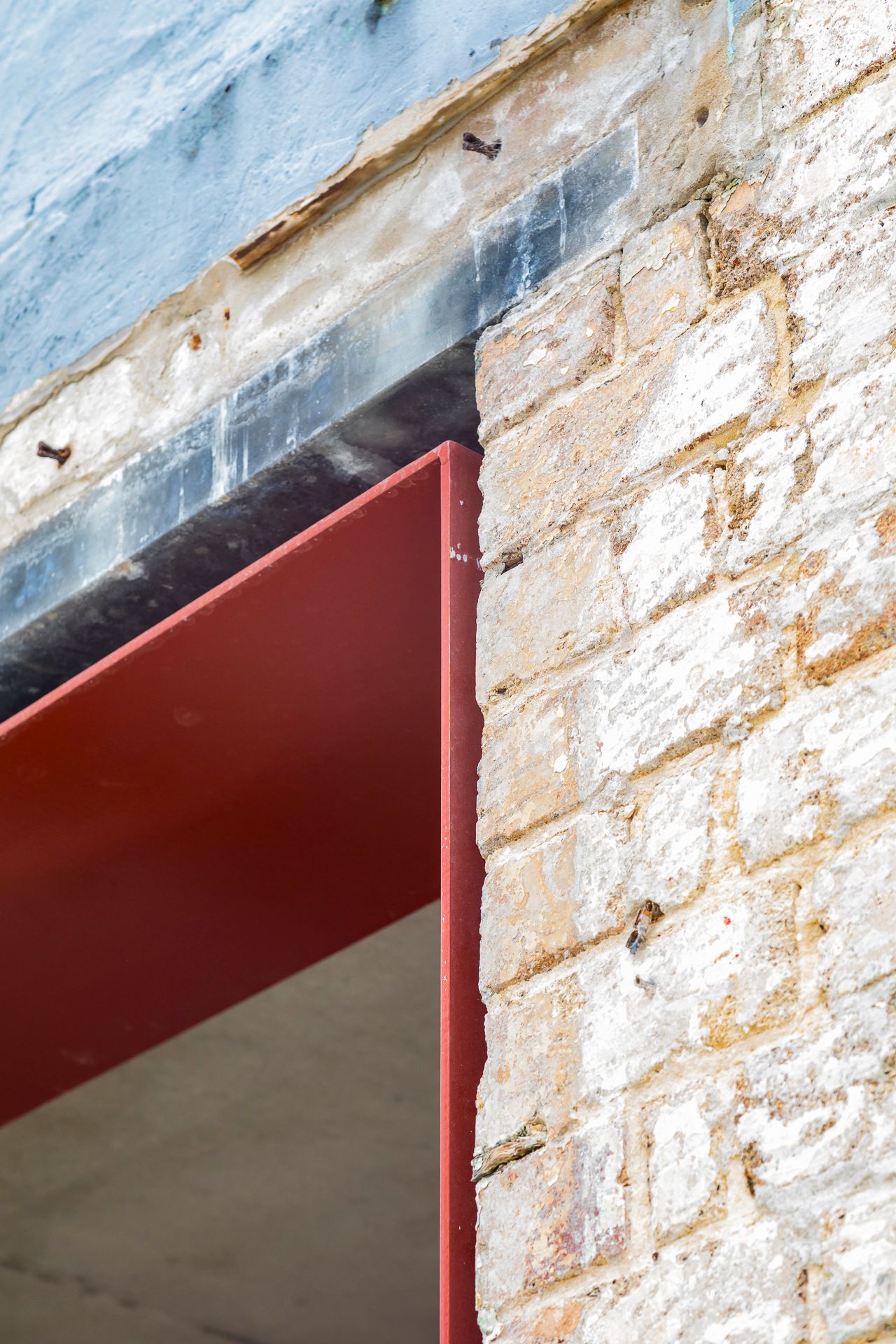Close-up of weathered sandstone brickwork above a window opening fitted with a bold red metal frame and dark lintel.