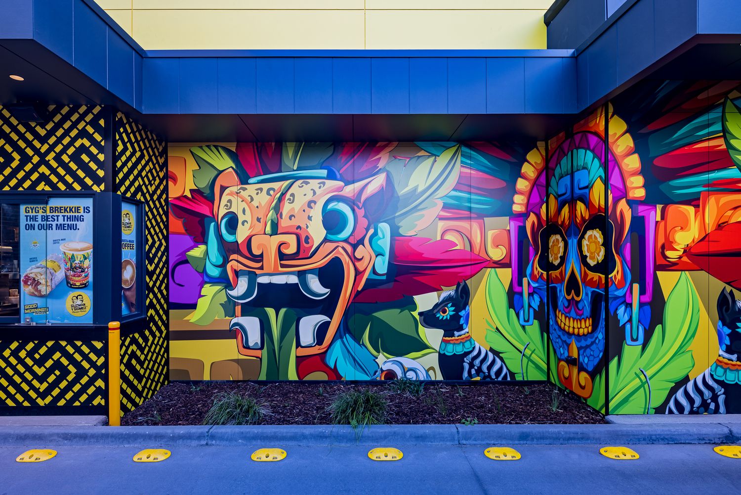 Colorful Aztec-inspired mural on the exterior wall of a Mexican restaurant, featuring a skull figure and vibrant patterns.