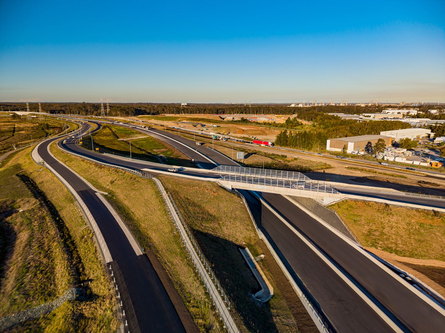Aerial view of a highway interchange with curving ramps and new asphalt lanes beside grassland at sunset.