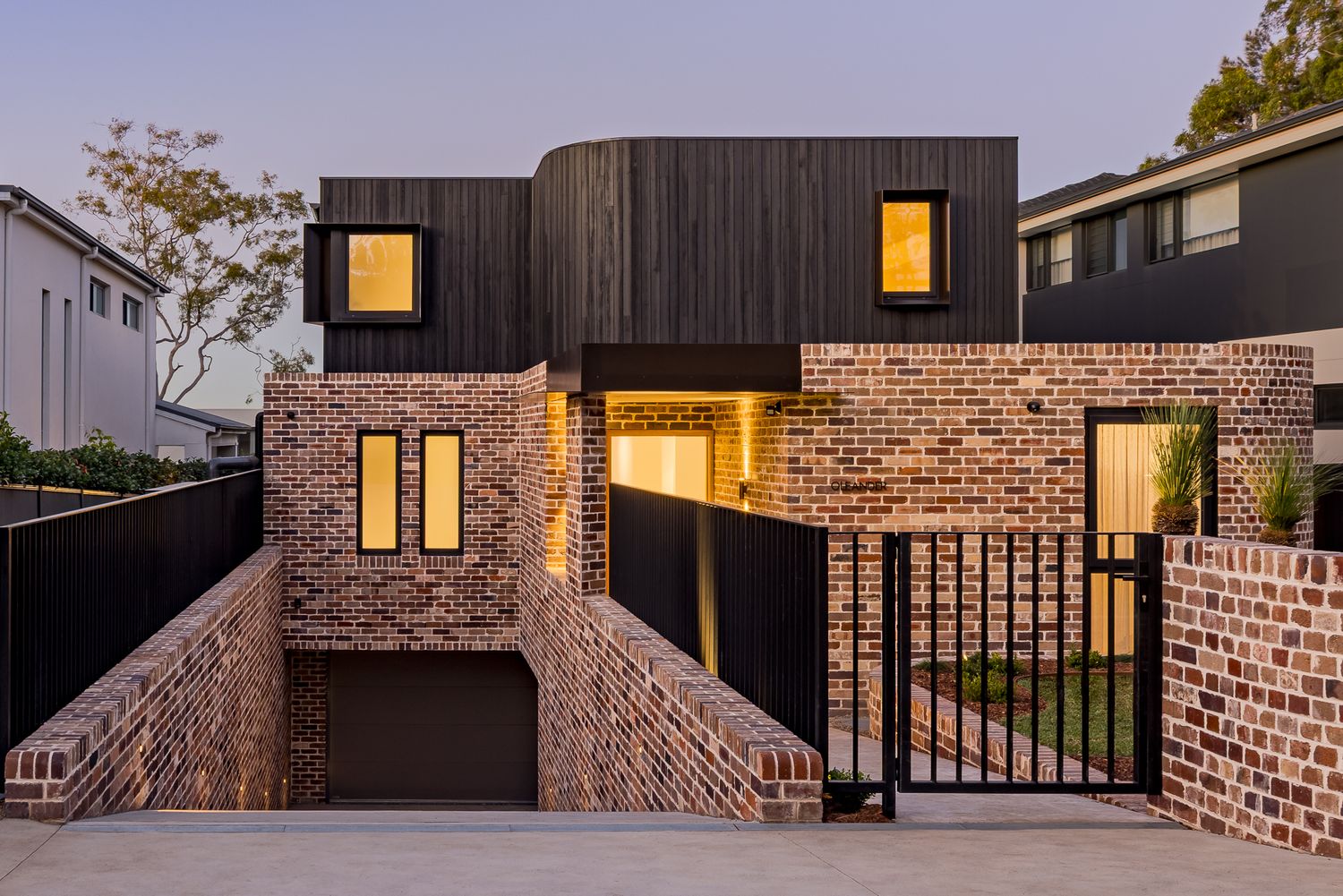 Contemporary two-storey brick townhouse with charred black timber cladding, a garage entry and a steel gate at dusk.