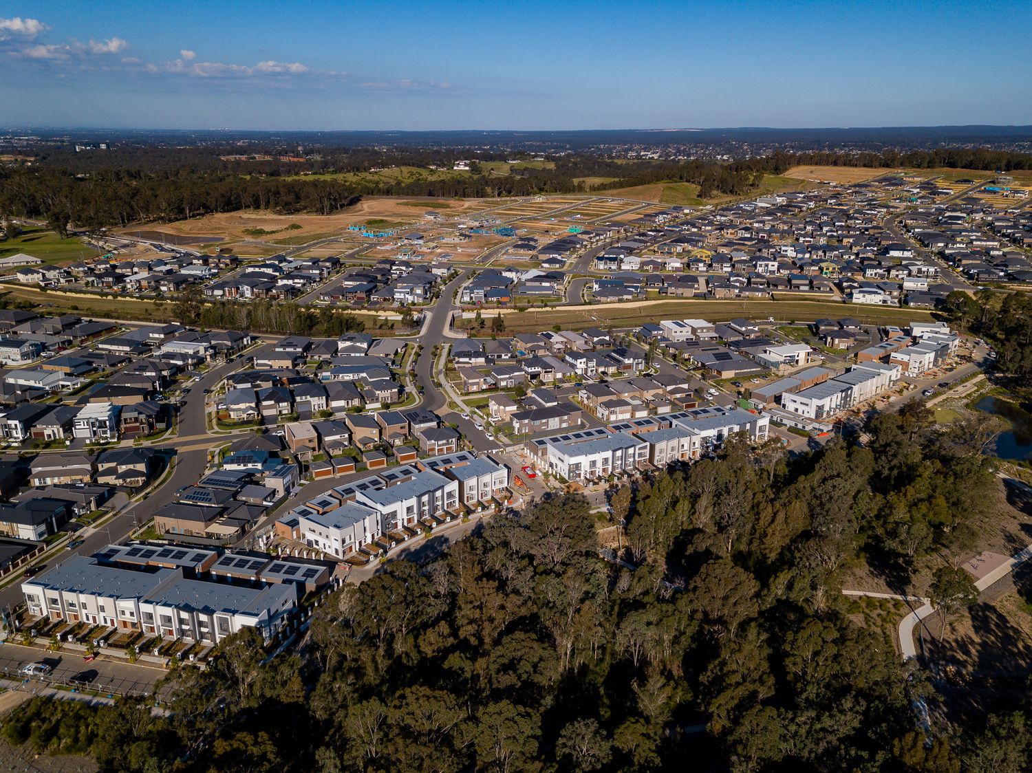 Aerial view of a sprawling new housing development with rows of homes, tree-lined bushland and cleared land stretching to the horizon.