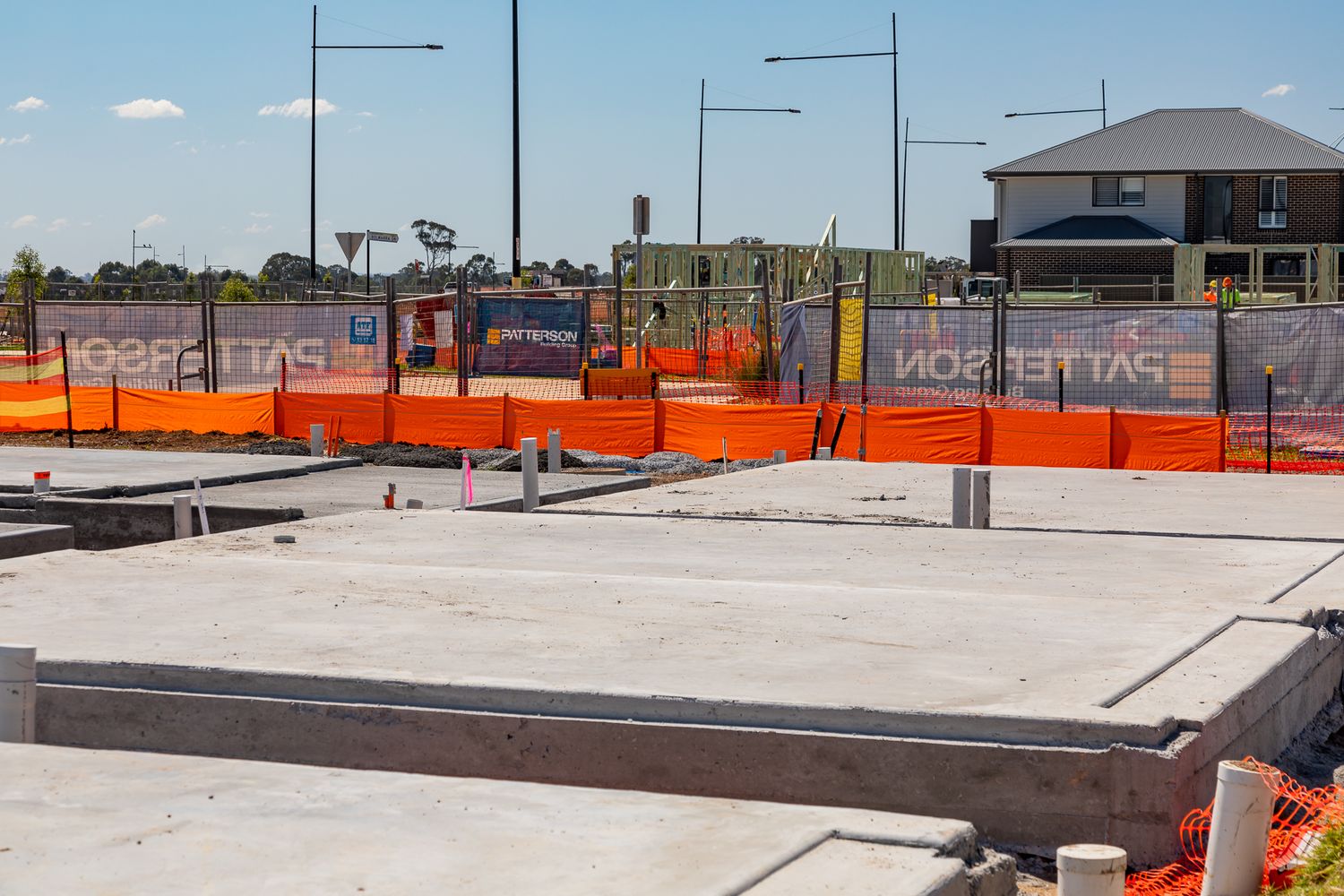Freshly poured concrete slab foundations with formwork edges and orange safety fencing at a residential construction site.