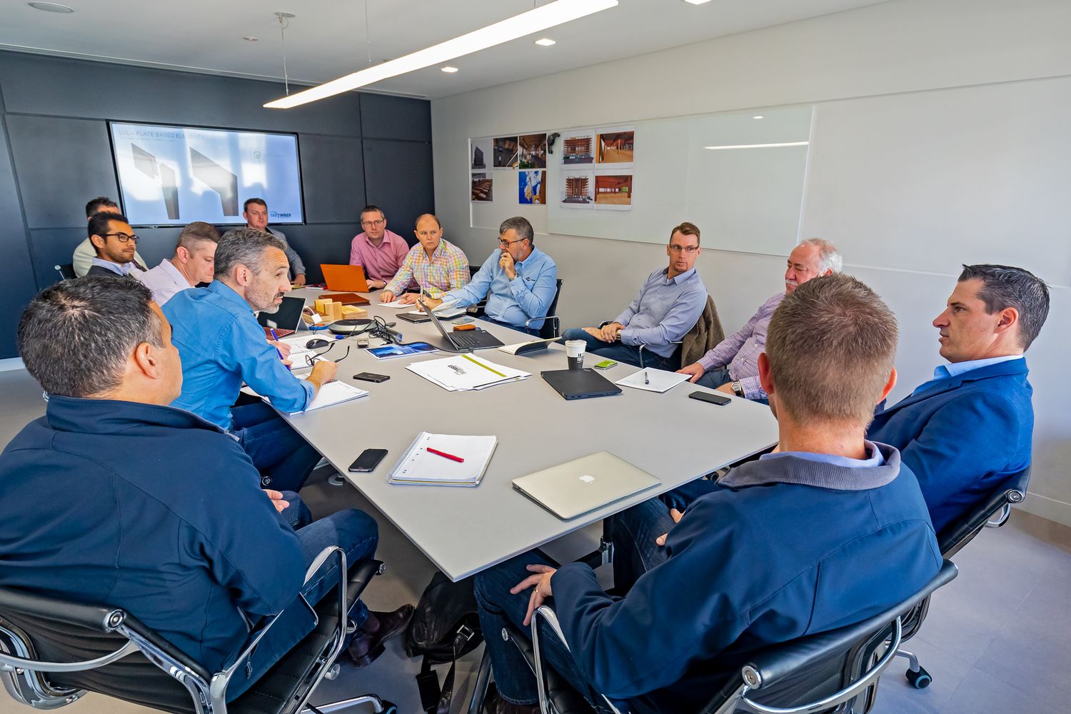 Business professionals in blue shirts sit around a large conference table during a team meeting in a modern office boardroom.