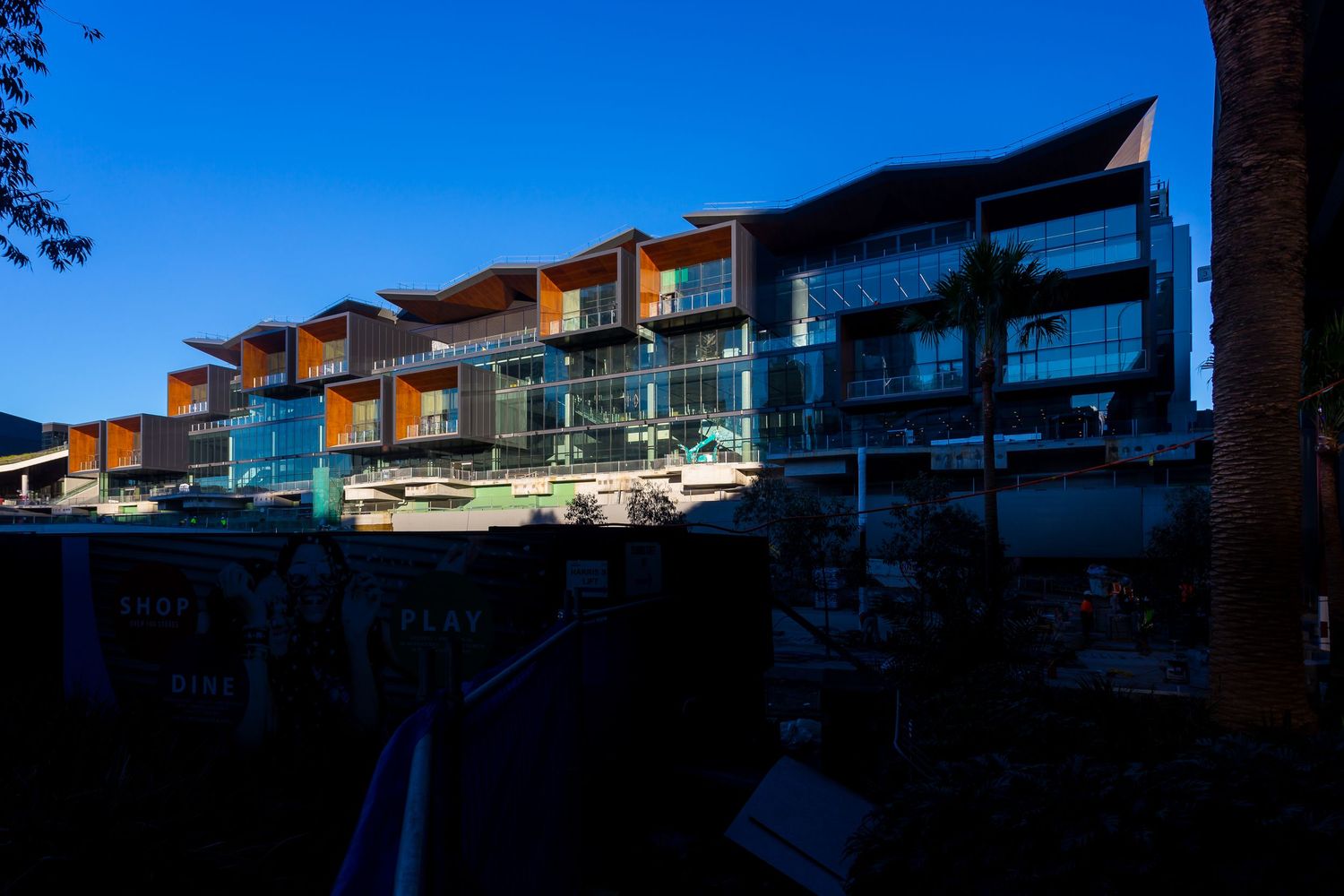 Modern multi-story waterfront building with terraced balconies and glass facades glowing against a deep blue twilight sky.