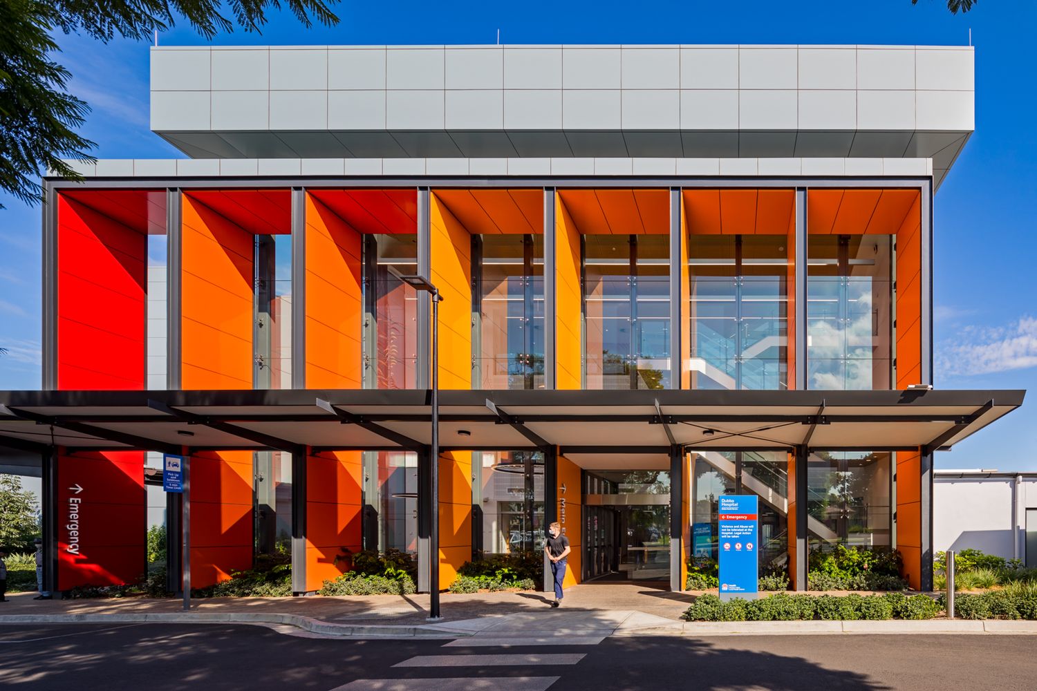 Colourful community building with red and orange vertical louvres, a cantilevered canopy and a person walking out front.