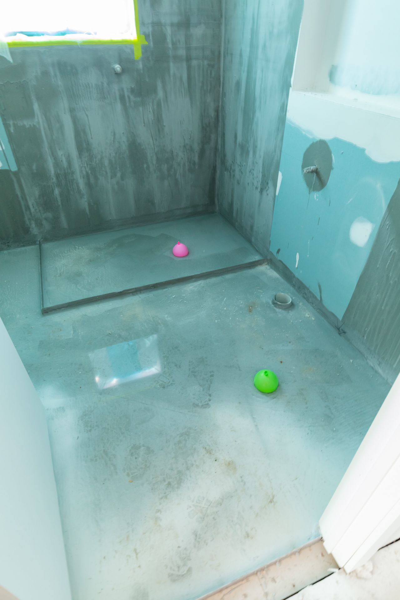 Bathroom under construction with waterproof membrane on the walls and shower floor, with two colourful balls on the surface.