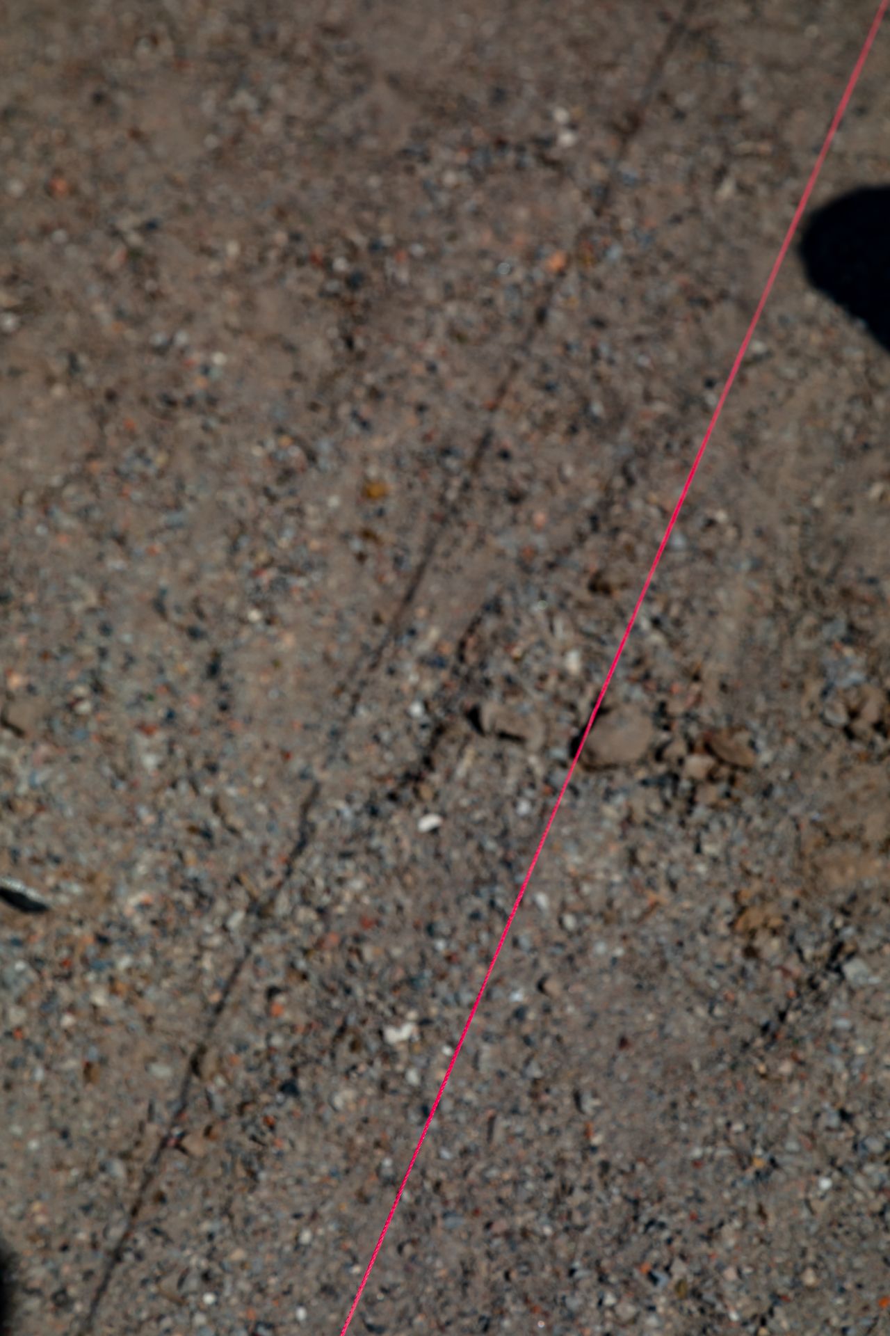 Close-up of a pink string line stretched across gravel and compacted dirt at a construction site marking a boundary.