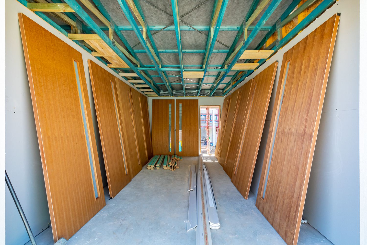 Timber roof framing and stacked wooden wall panels inside an unfinished garage space of a new home under construction.