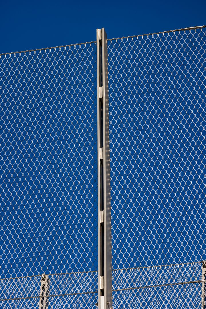 Chain-link fence with a vertical metal post against a deep blue sky.