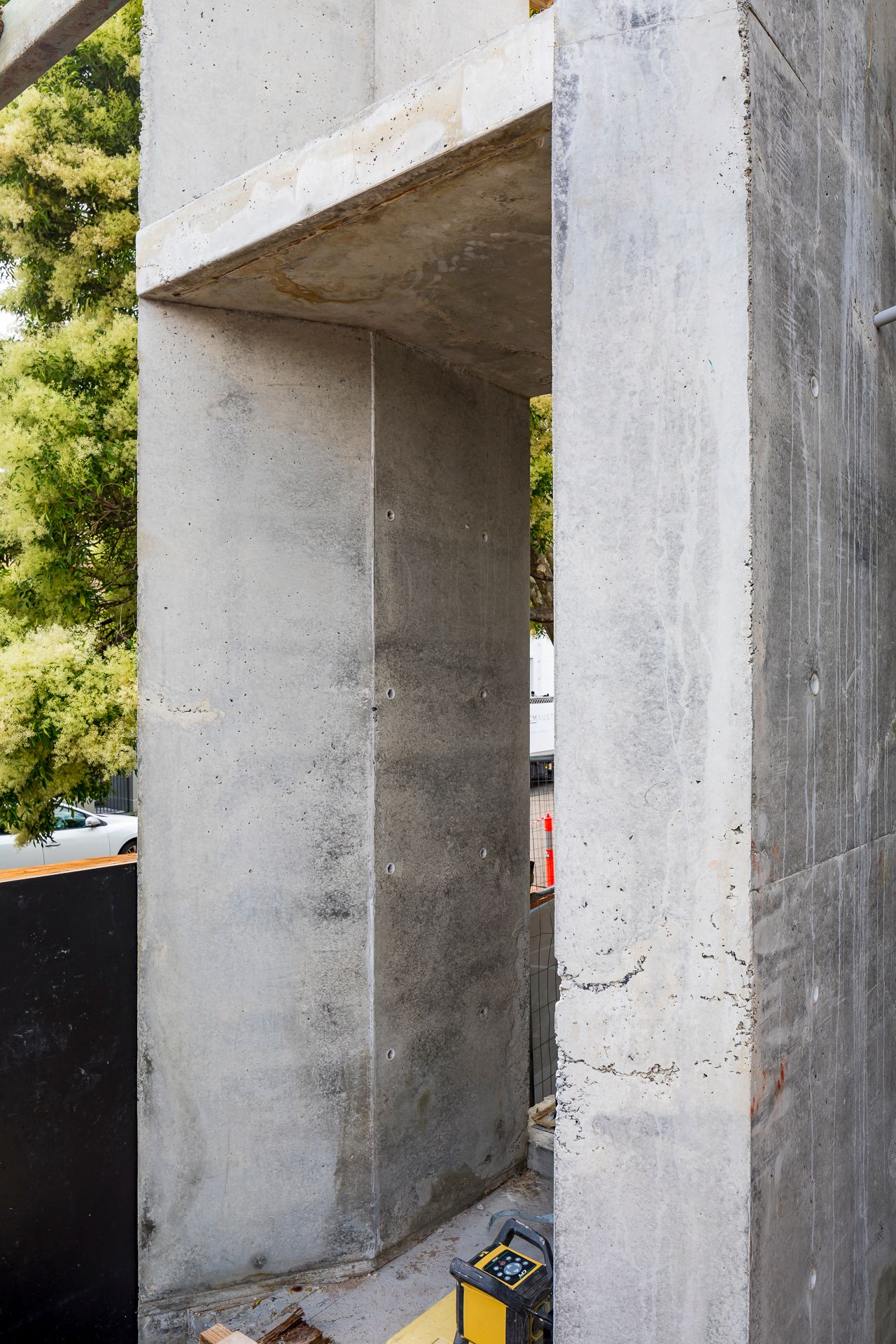 Exposed concrete walls and overhead slab forming a doorway-like opening on a construction site with a laser level at the base.