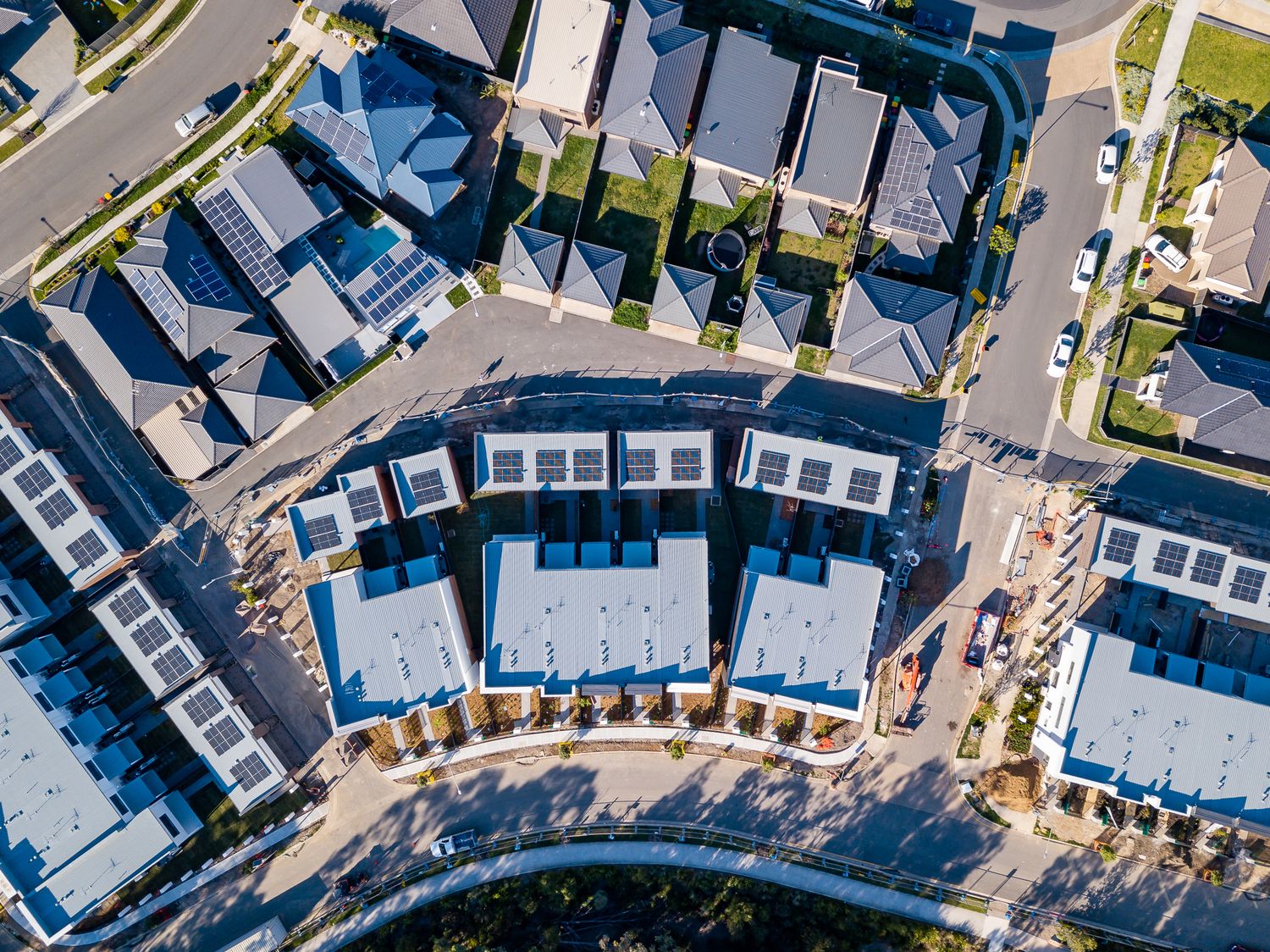 Aerial view of a modern townhouse development with rows of new homes, solar panels and landscaped streets.