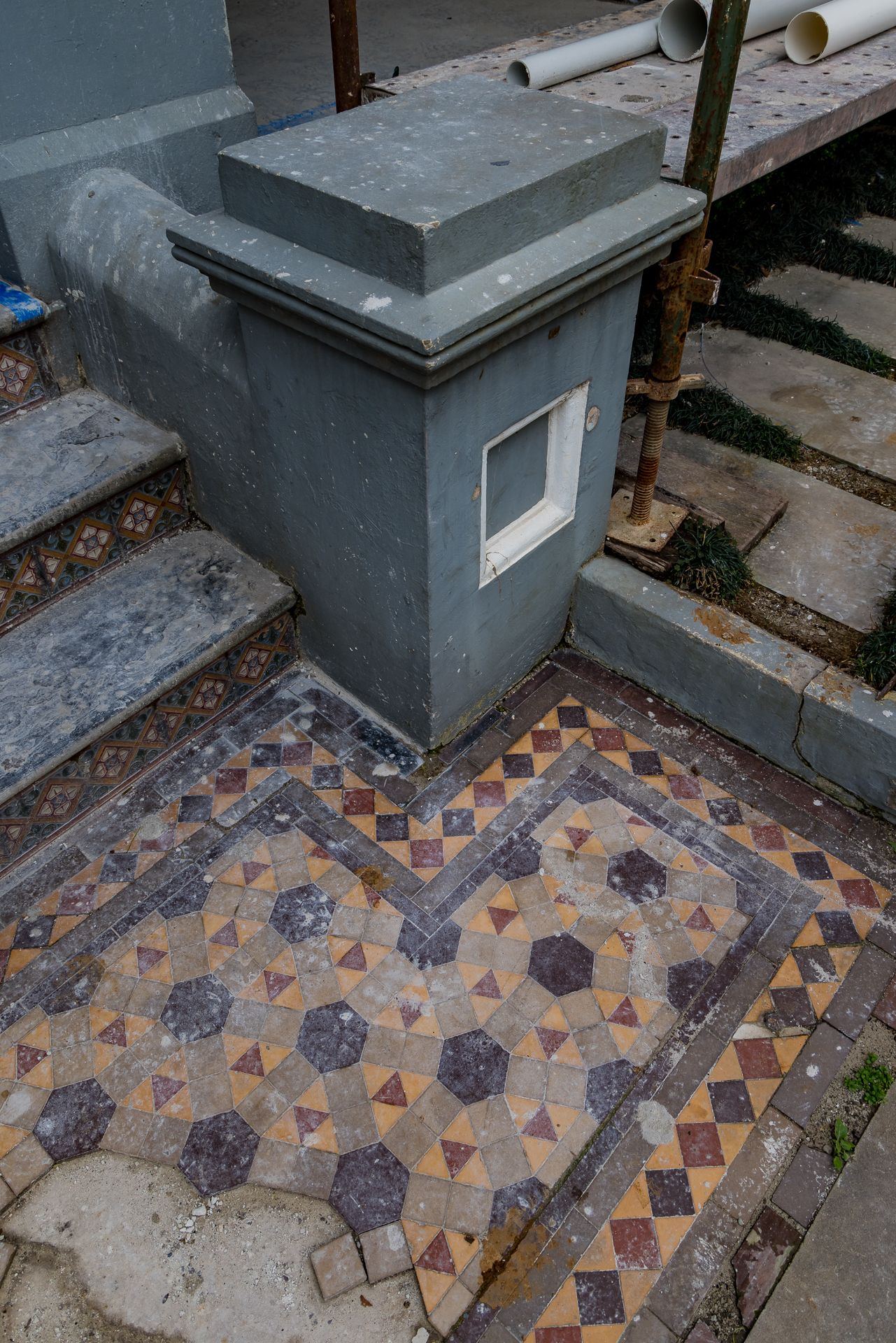 Heritage entry steps with a grey rendered pillar and a geometric Victorian mosaic tile floor in muted red and charcoal.