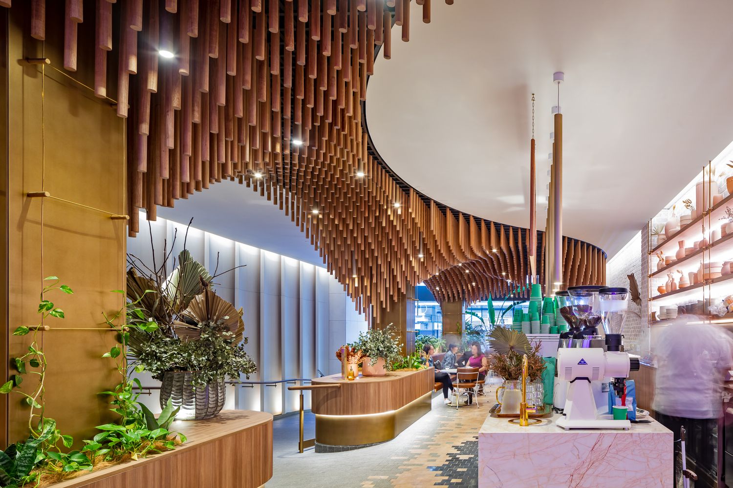 Curved timber ceiling installation flows over a stylish cafe with planter boxes, an espresso machine and guests seated in the background.