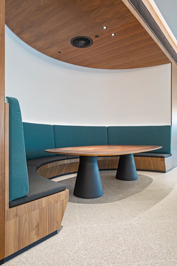 Curved teal upholstered booth seating around a round walnut table beneath a timber ceiling in a modern interior.