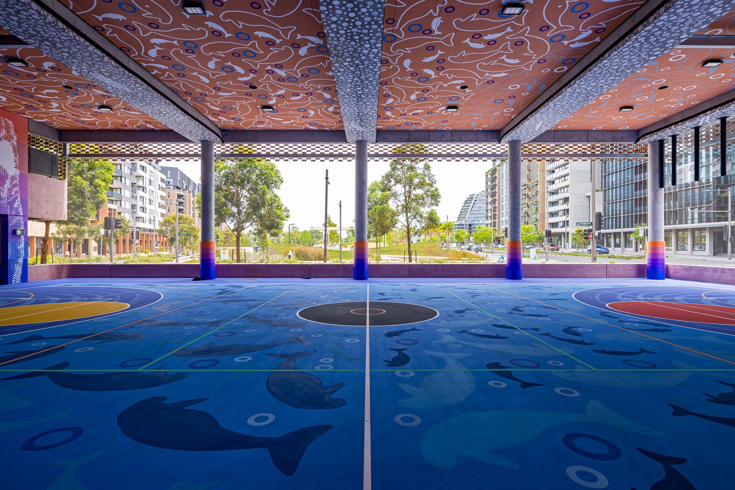 Blue sports court painted with whale and sea creature artwork beneath a decorative orange perforated ceiling and colorful columns.