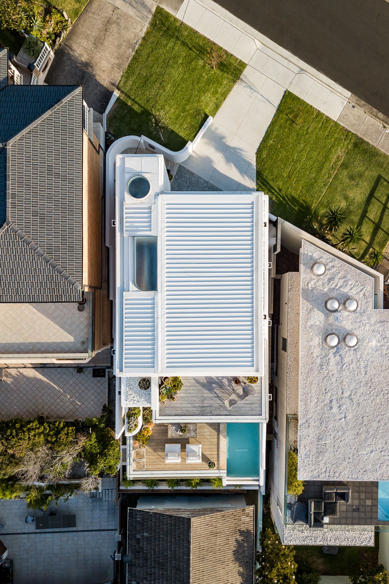 Top-down drone view of a modern white house with a skylight, rooftop terrace, and blue pool.